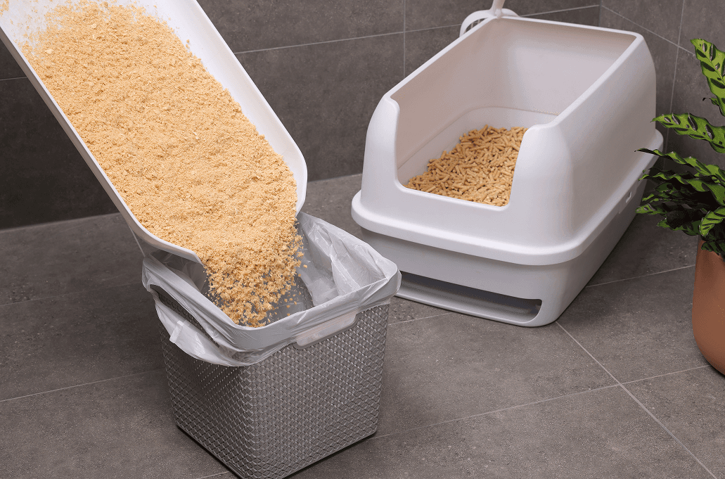 A Treasured Pals Premium Sifting Litter System with a separate container of fresh litter being poured into a plastic-lined basket, set against a tiled floor with a potted plant nearby.