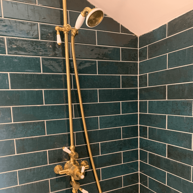 Brass shower fittings in green metro tiled shower enclosure