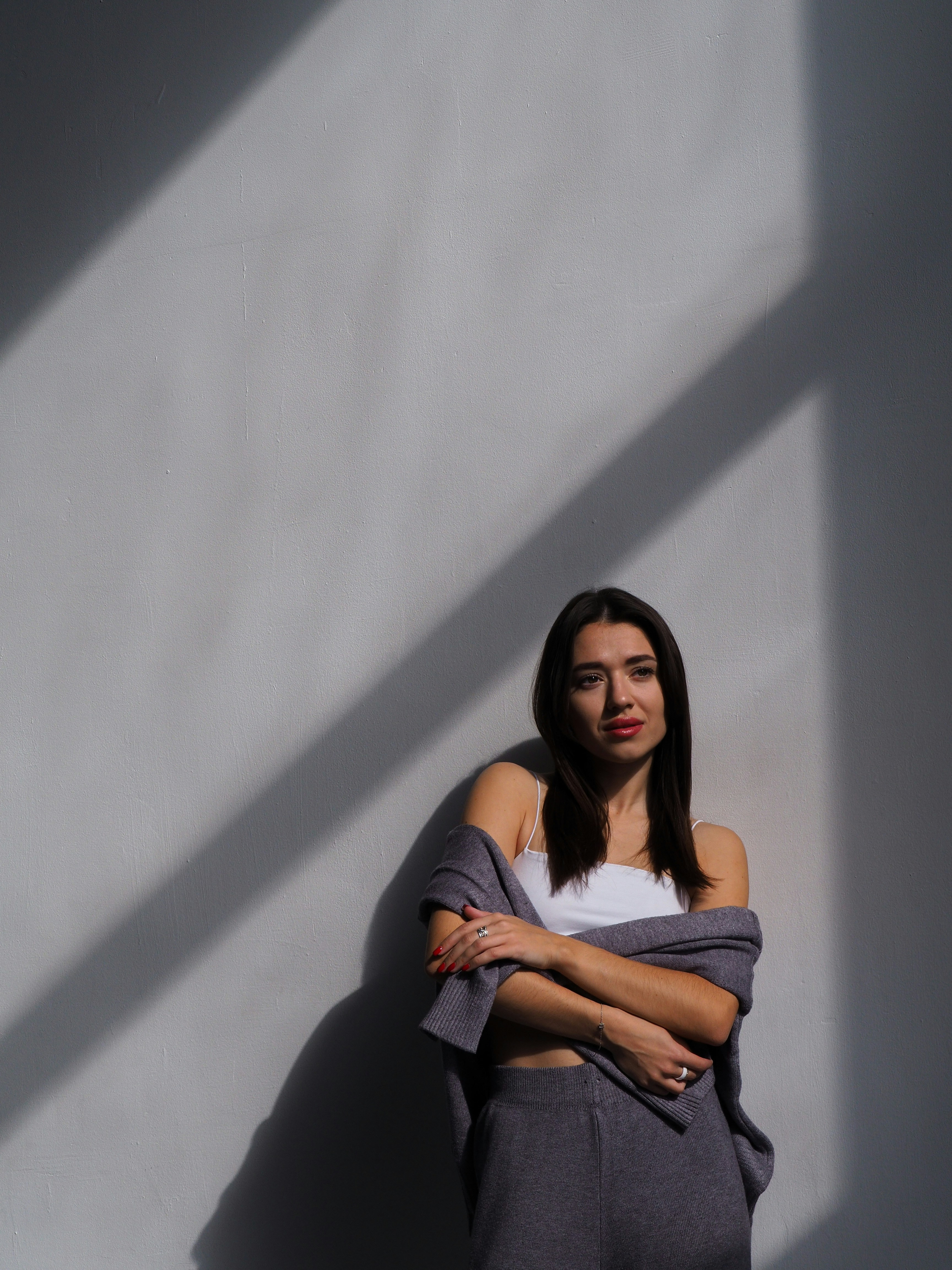 A woman in loungewear stands against a wall with shadows.