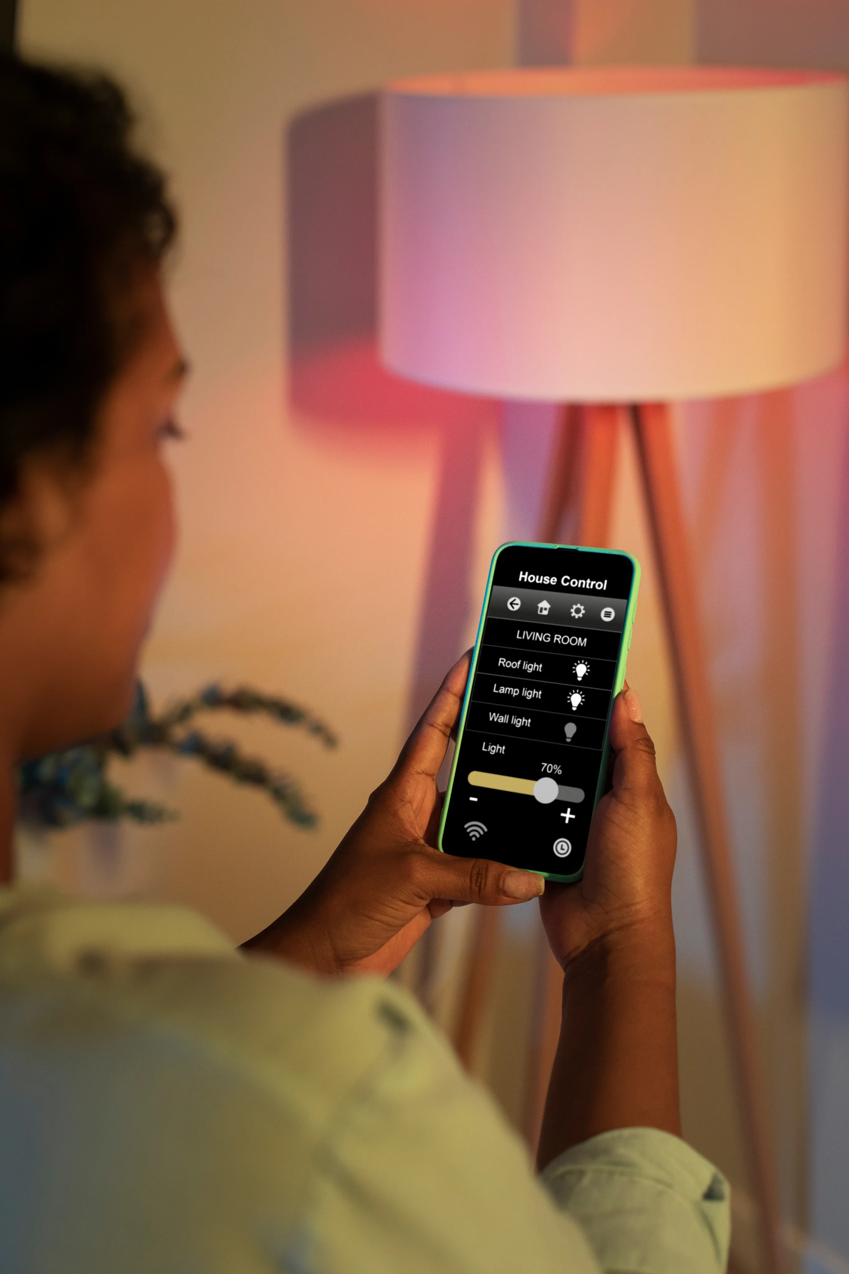 Close-up of a person holding a smartphone to adjust smart lighting brightness with a floor lamp in the background.
