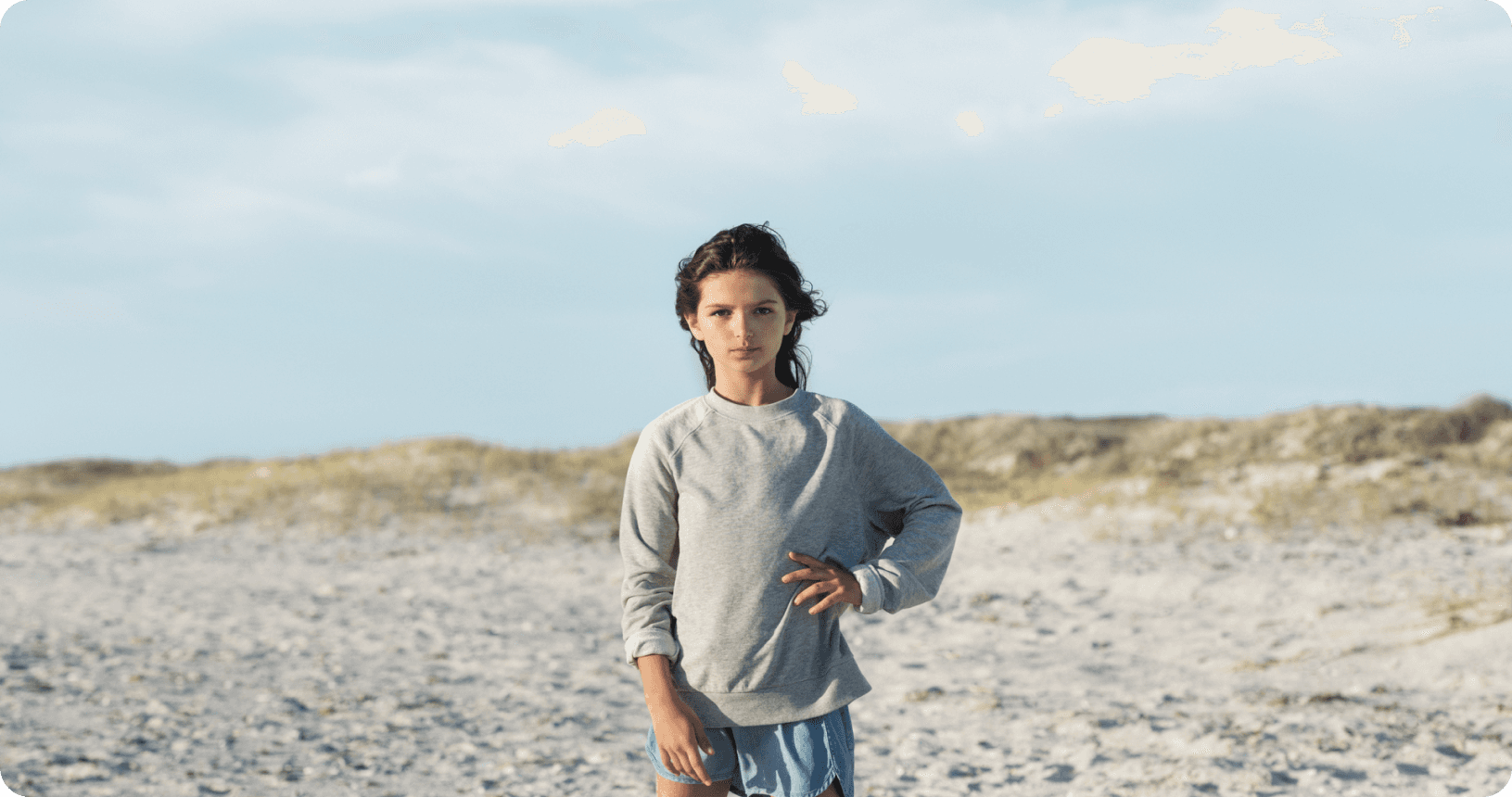 Persoon op het strand met duinen en zee op de achtergrond.