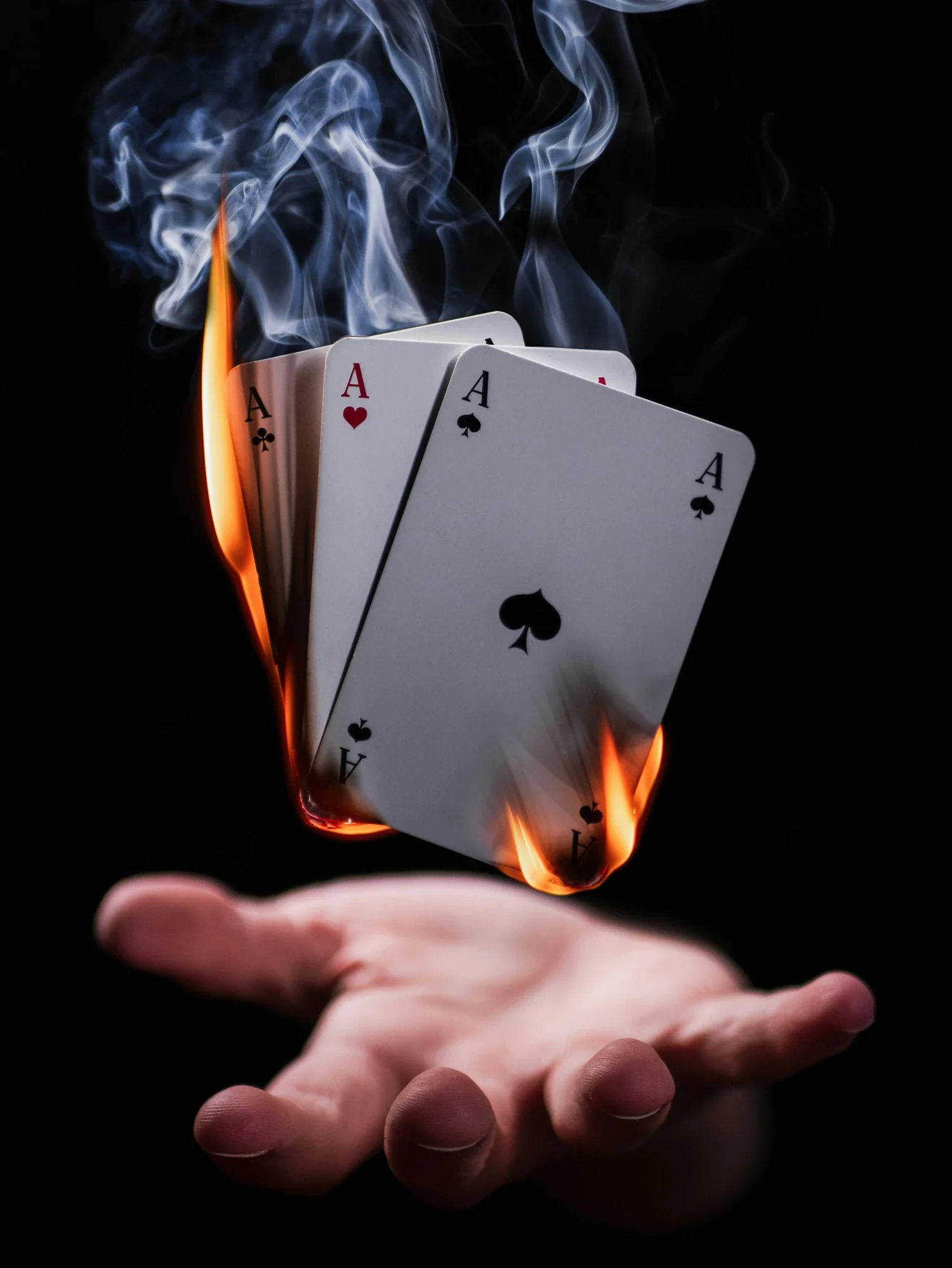 Four aces burning in flames hover above an open hand against a black background.