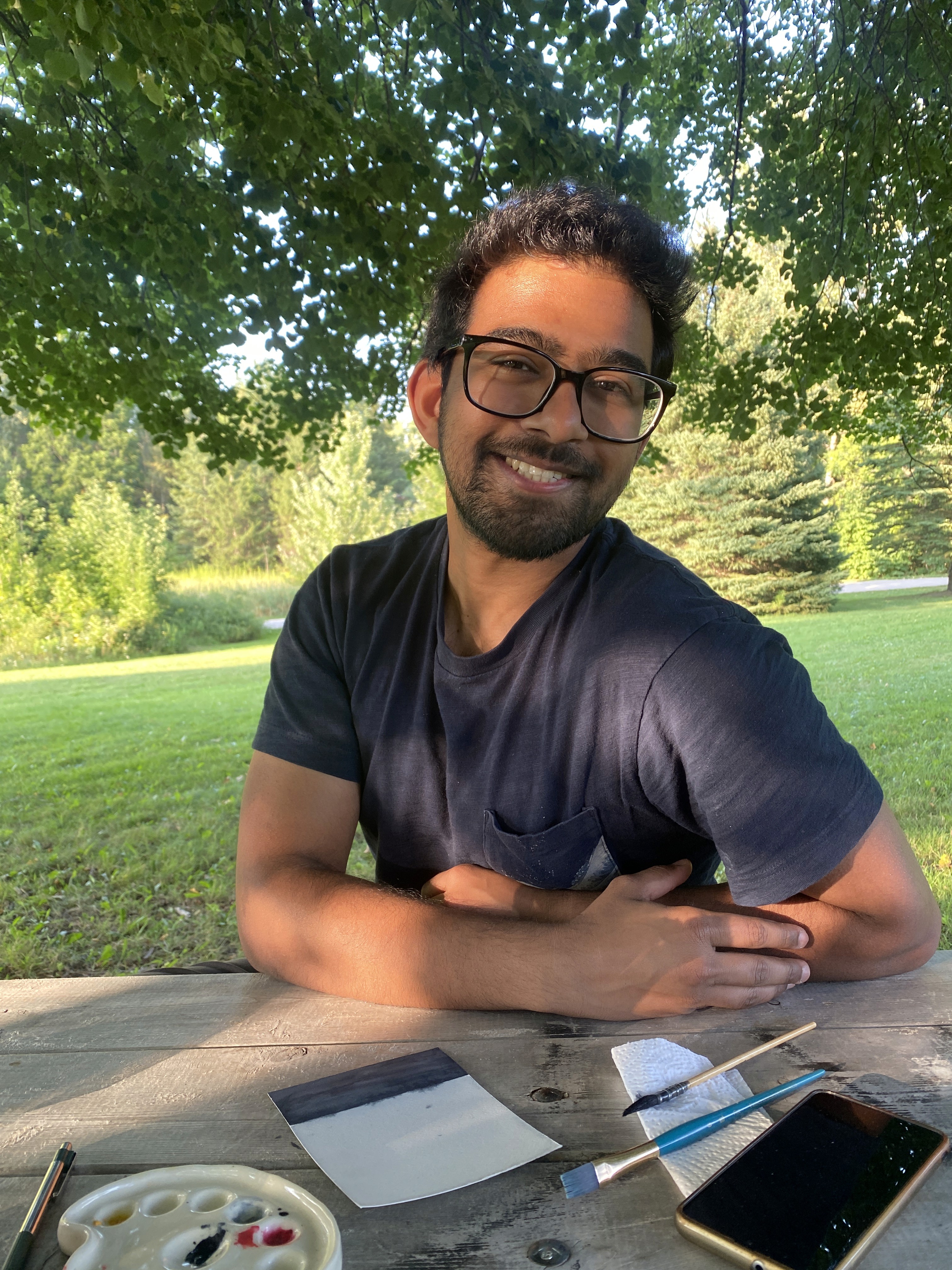 Rahul, co-founder and website designer at Visual Mess Studio — seated outdoors with a watercolor paper, specialising in Framer website design and brand strategy for creative small businesses