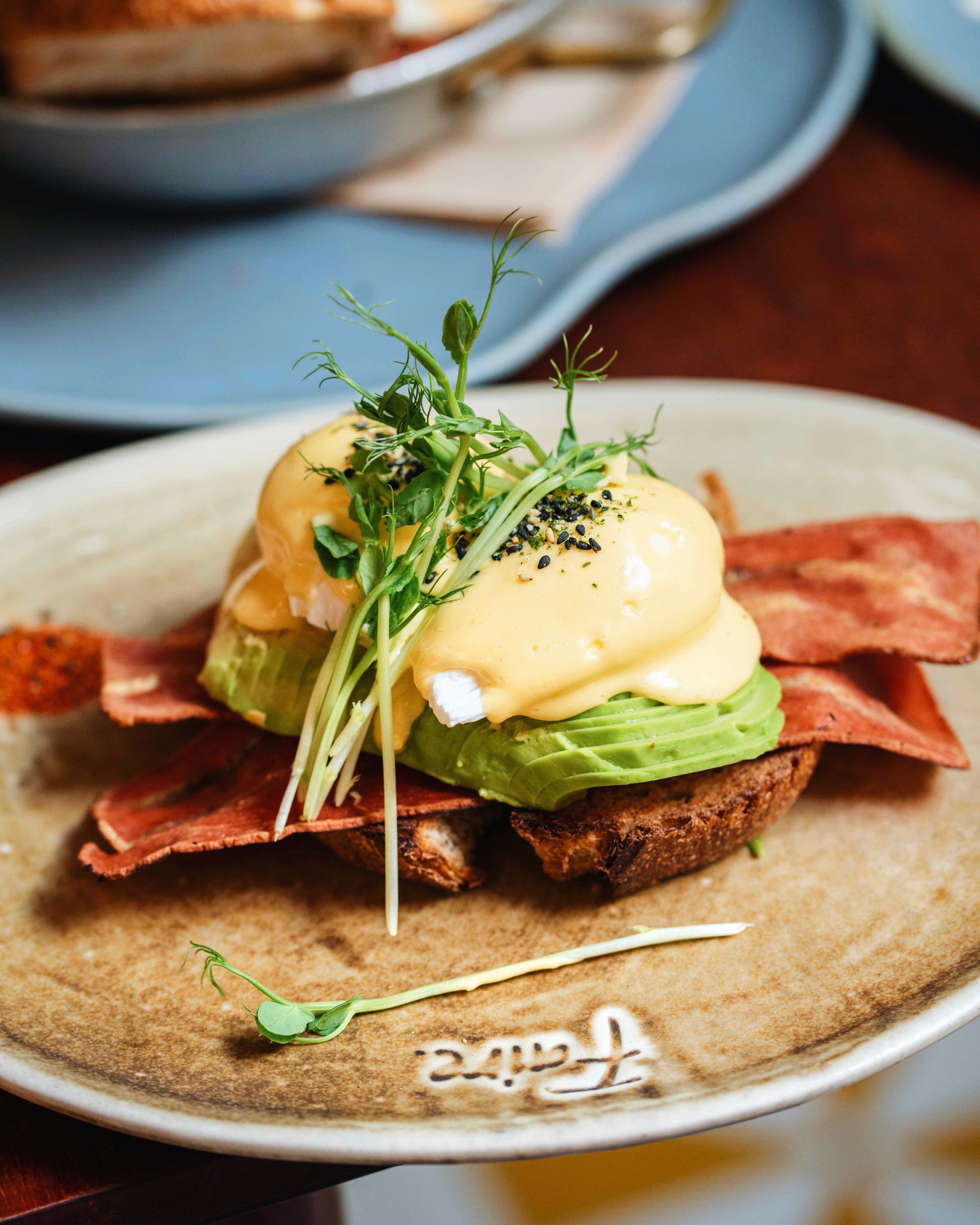 Vegetarian eggs Benedict with avocado, plant-based bacon and microgreens on a branded Faire plate — brunch at Faire. Brunch & Drinks, Eixample Barcelona