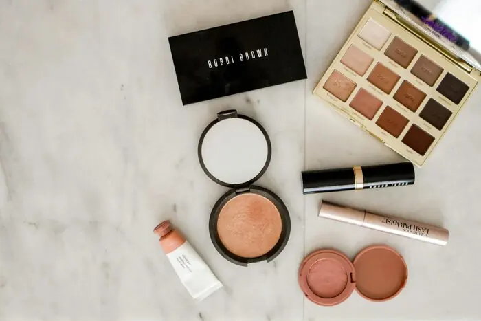 An assortment of makeup products, palettes and compacts arranged on grey marble