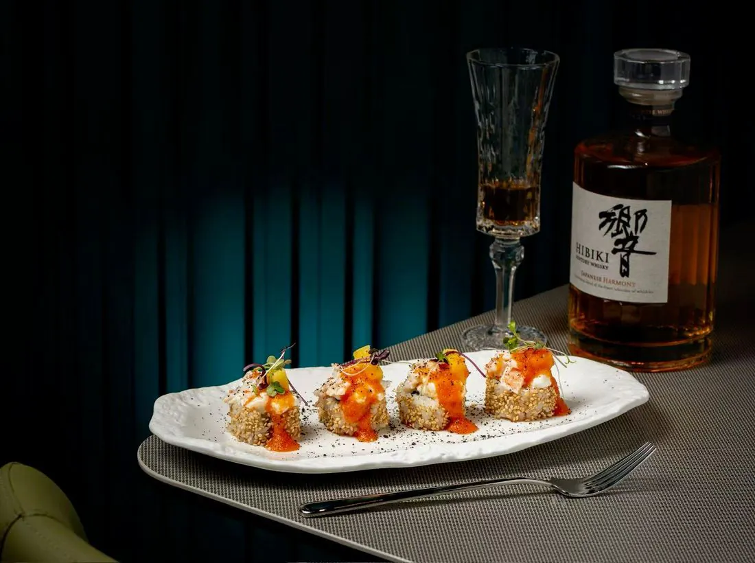 Makis au saumon et coupe de champagne, devant une bouteille de whisky japonais