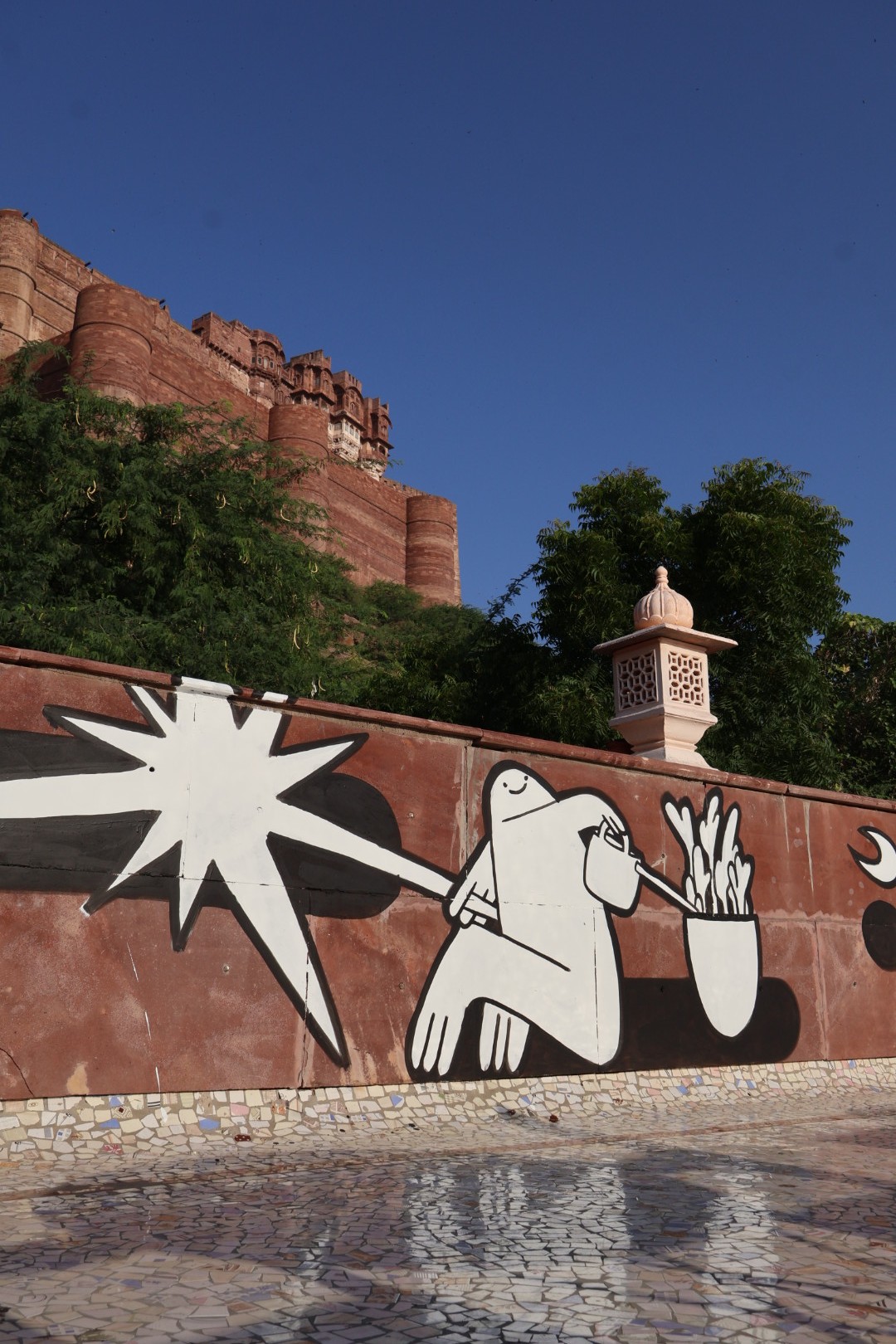Mural painting with joyful cartoon characters and the word ‘Hello, नमस्ते, سلام عليكم’ painted on a terrace of a blue building near Jodhpur Fort.