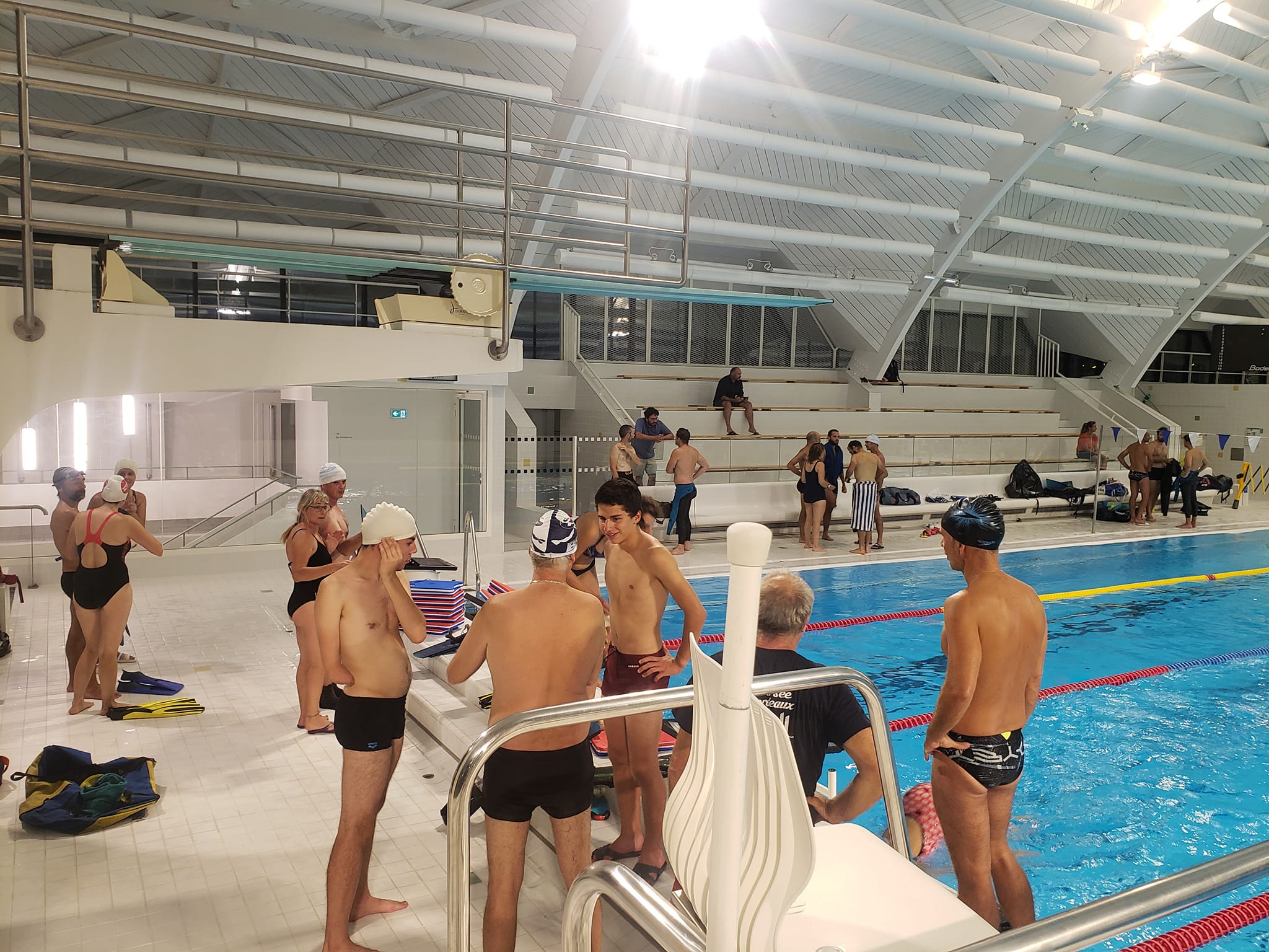 A young person with curly hair smiles at the camera while sitting in front of a laptop against a dark background.