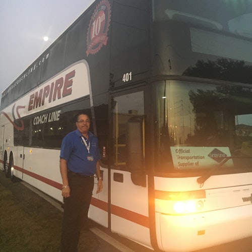 En person i en blå skjorta står bredvid en dubbeldäckare från Empire Coach Line. En skylt lyder, "Officiell transportleverantör."