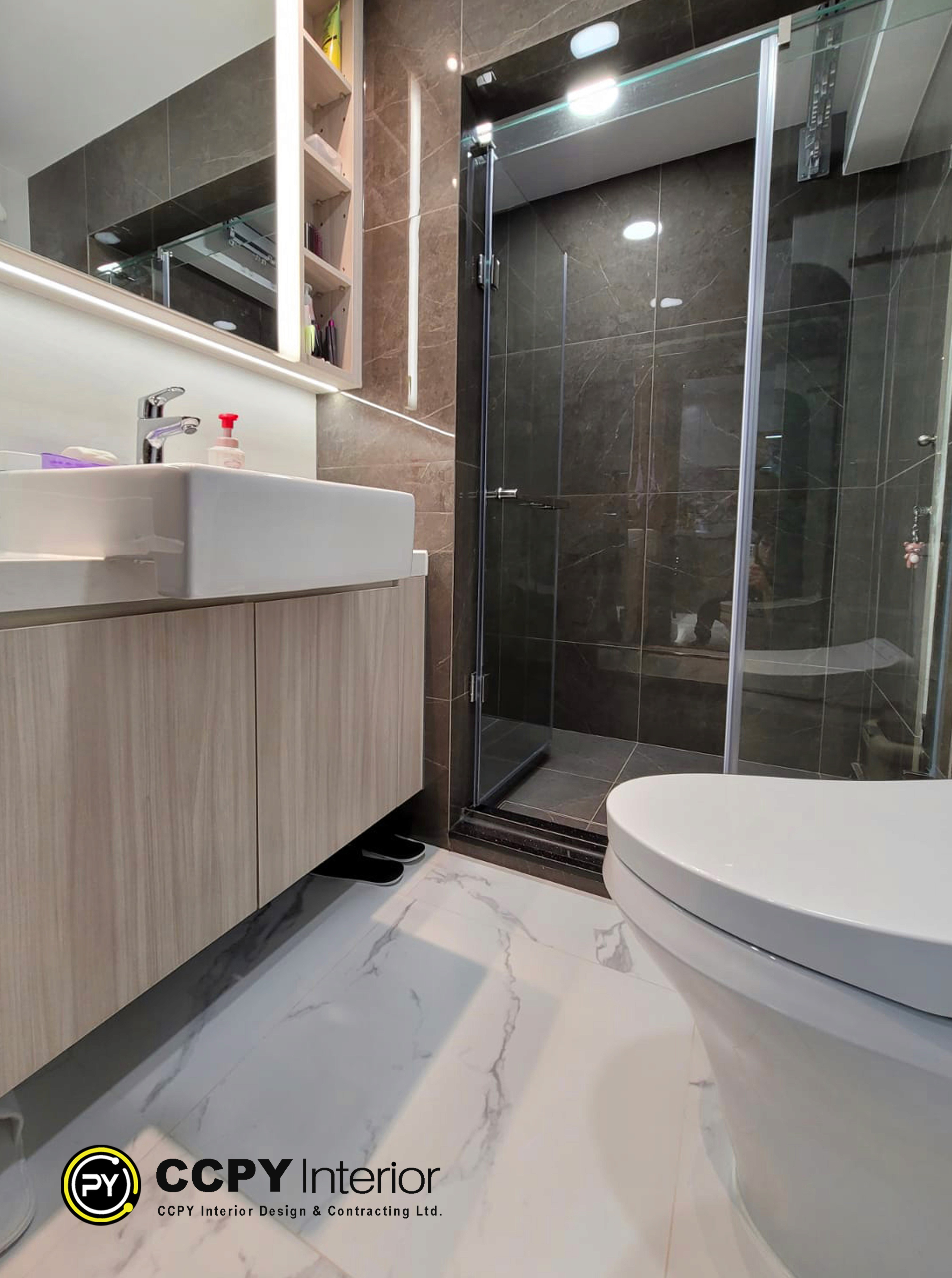 This is a modern bathroom featuring a floating wooden vanity and a walk-in glass shower enclosure.Vanity: The bathroom includes a light-wood grain floating cabinet with a white rectangular vessel sink.Shower: A walk-in shower is enclosed by a glass door and features dark, textured tiles on the walls and floor.Fixture Details: The shower entrance is framed by a sleek silver metal edge, and dark slippers are visible beneath the vanity