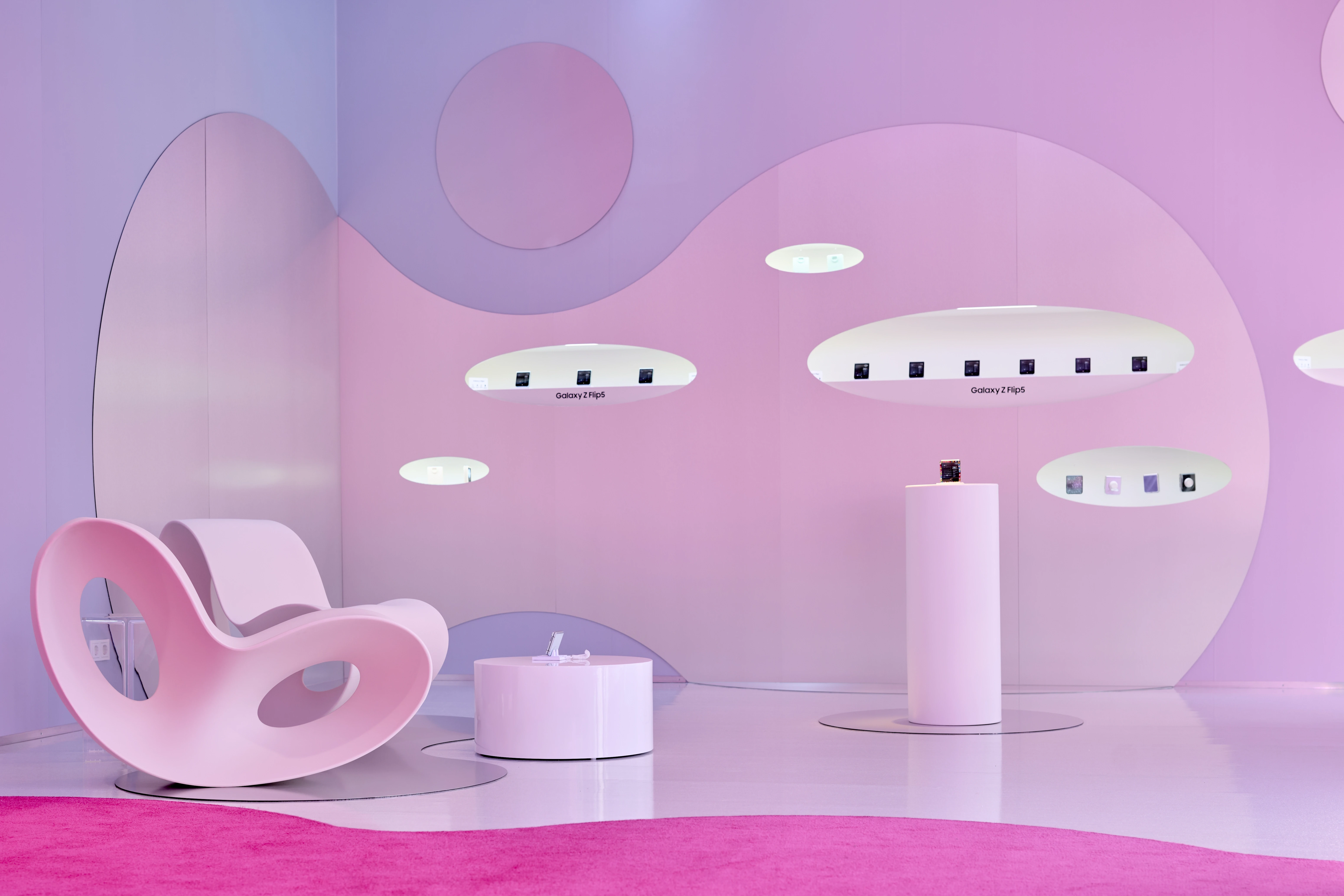Galaxy Z Flip phones in glowing oval wall niches beside a pink rocking chair and pedestal at the Samsung Flipside pop-up.