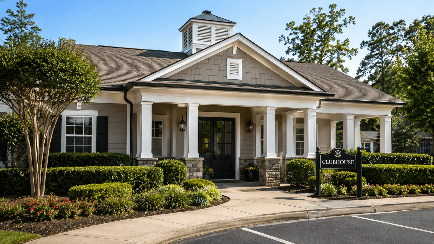 HOA clubhouse exterior with columns, trim, entrance doors, and landscaped common areas