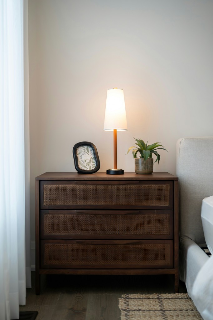 A wooden nightstand with a lamp and plant.