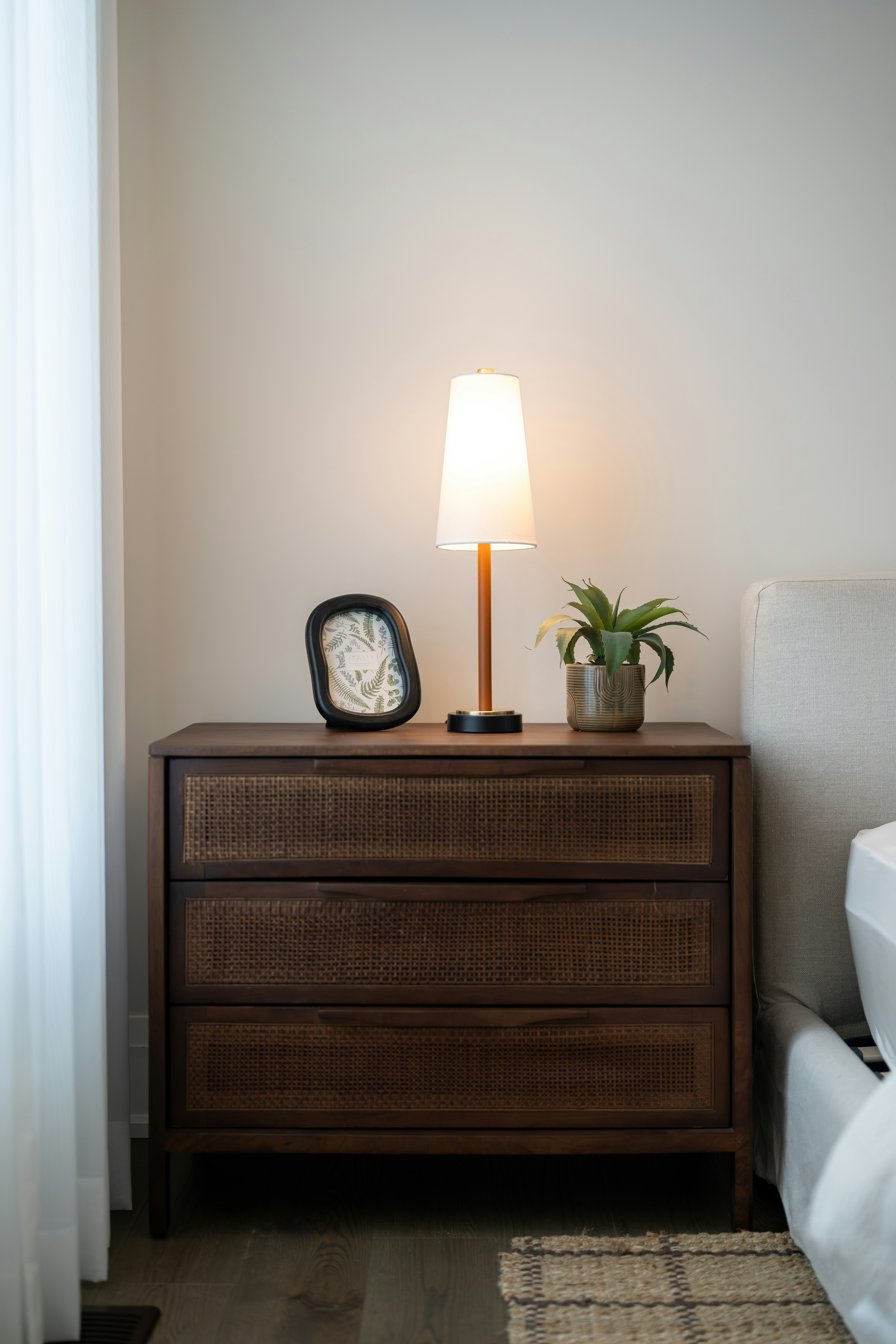 A wooden nightstand with a lamp and plant.