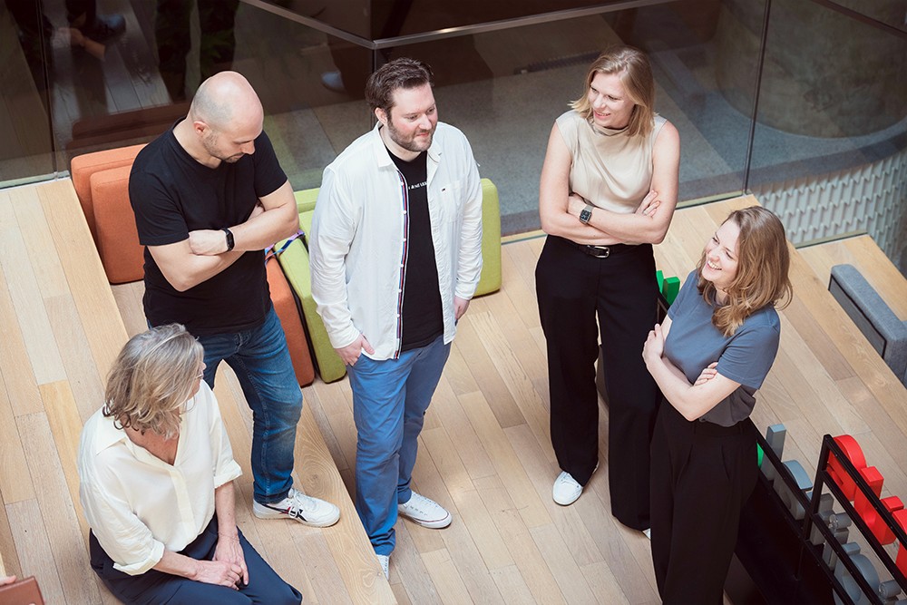 A decorative image featuring the Videodock team engaged in conversation. Several team members are depicted standing or seated in a circle, facing each other and engaged in discussion. 