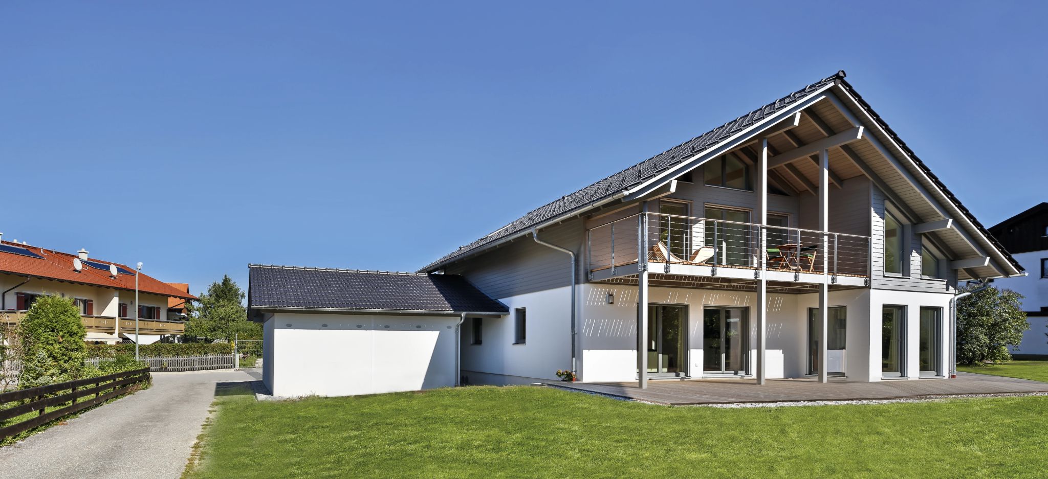 Modernes Einfamilienhaus mit Garage, Terrasse und Balkon an einem sonnigen Tag.