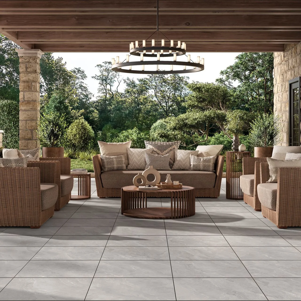 Covered patio with cushioned seating, a round coffee table, pale paving and a view of leafy trees.