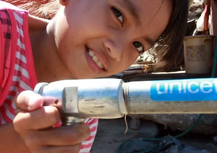 Ein lächelndes Kind an einer UNICEF-Wasserpumpe – Die DAG Unternehmensgruppe unterstützt UNICEF-Projekte zur Sicherung der Trinkwasserversorgung weltweit.