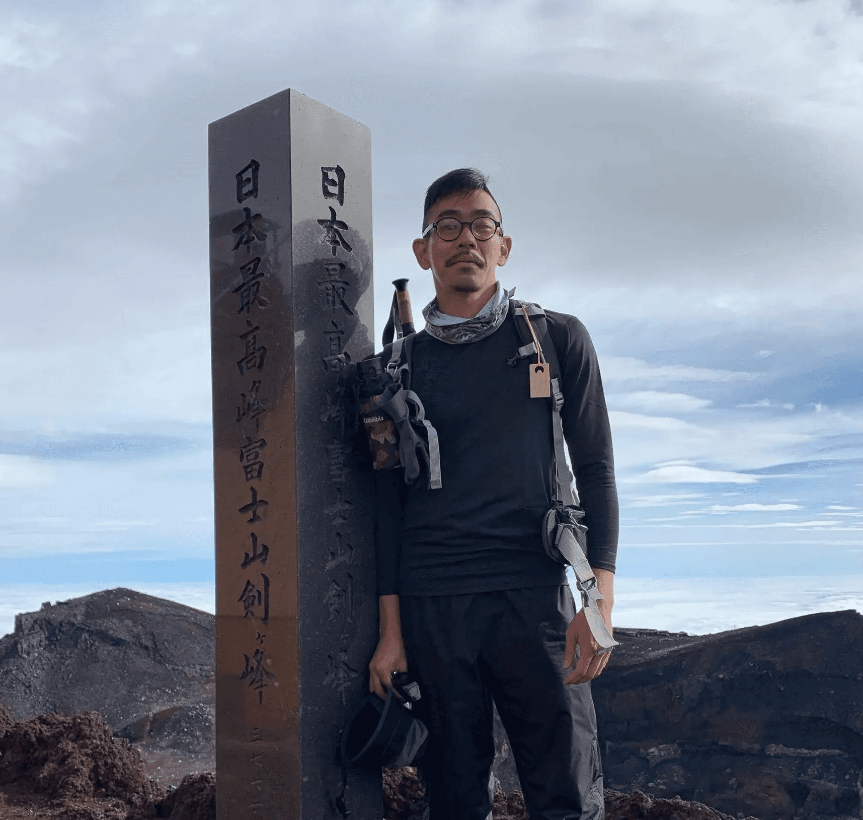 A male person leaning on a pole indicating the summit of Mt. Fuji