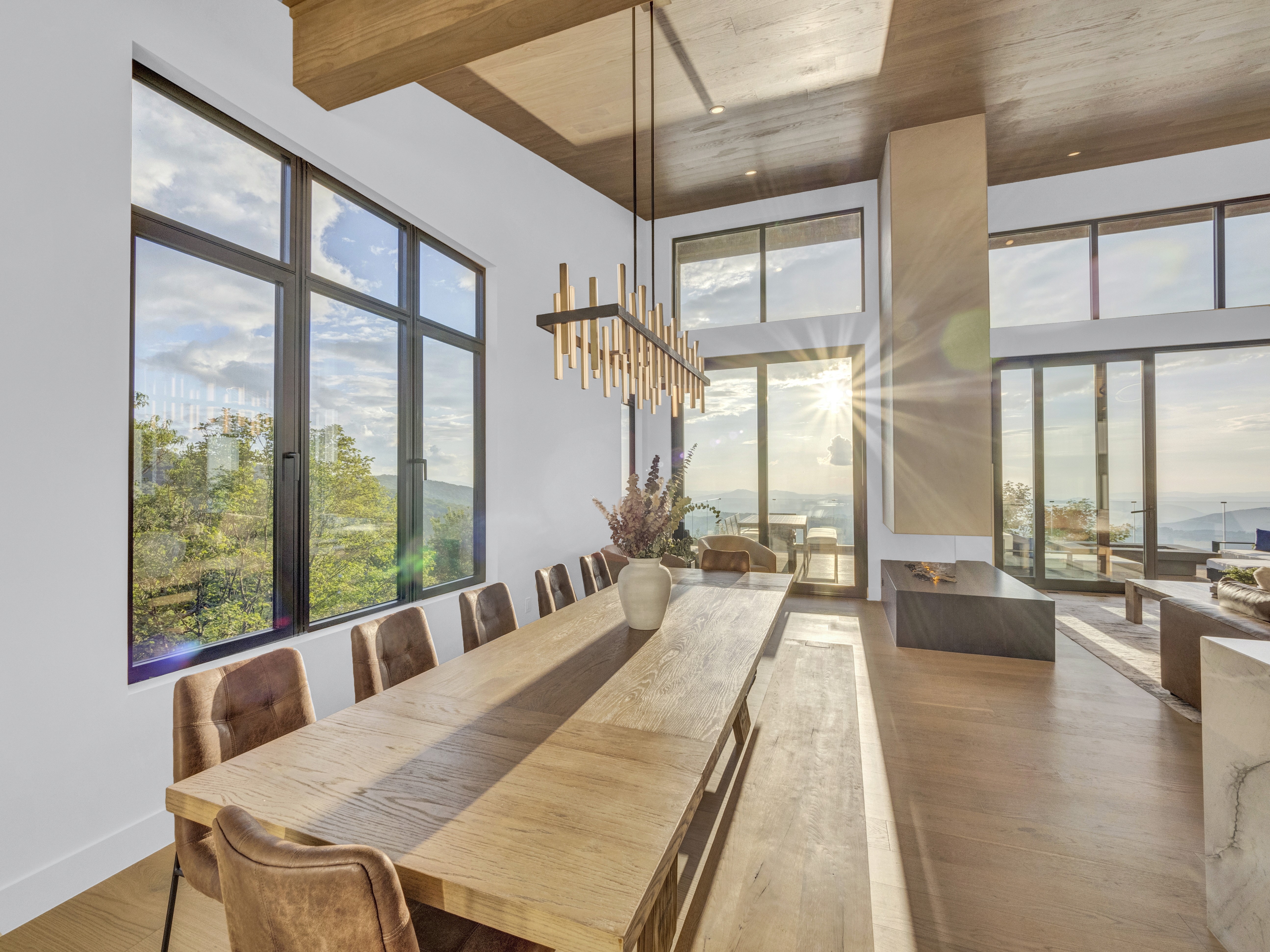 The dining area bathed in golden hour light, with a sunburst effect coming through the massive mountain-facing windows