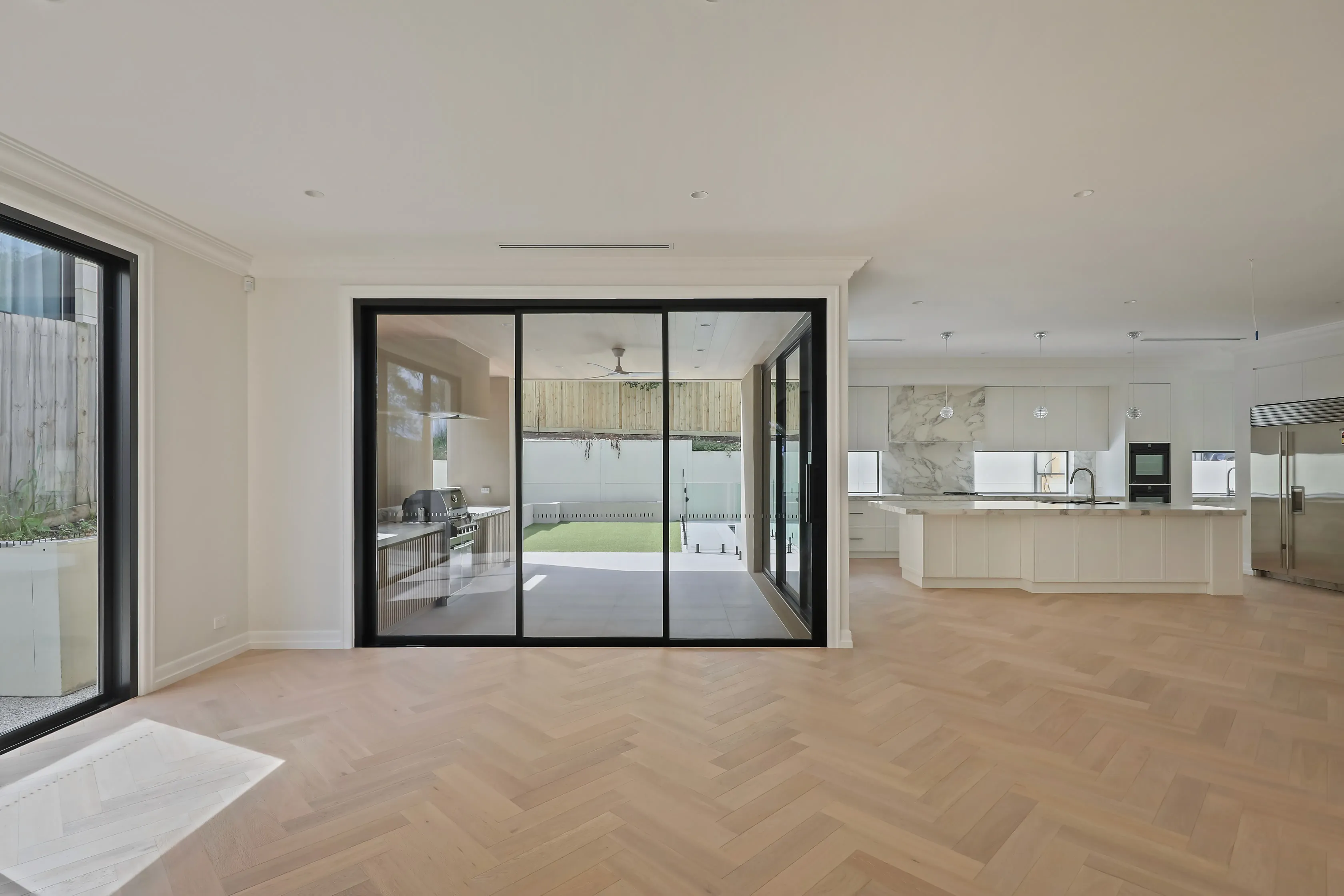 Templestowe open living area with herringbone parquet and black steel-framed sliding doors opening to a courtyard with pool and barbecue