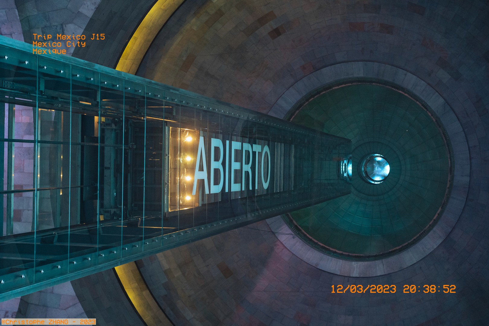 Perspective du Monument à la Révolution à Mexico avec un panneau "Abierto" en lumière.