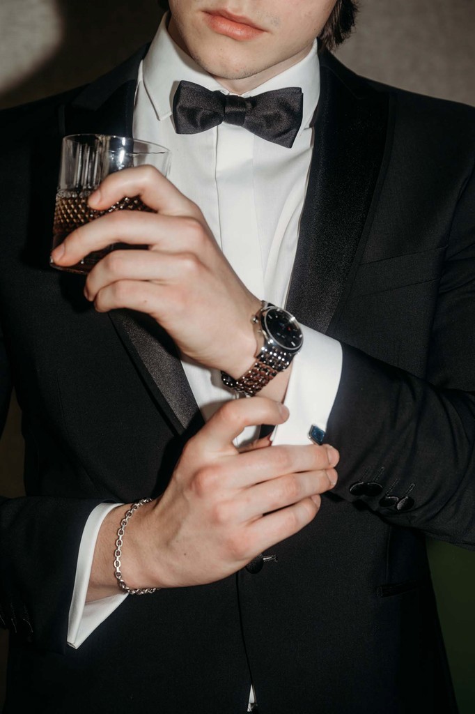 Mann im Anzug der sich den Manschettenknopf richtet und ein Whiskey Glas in der Hand hält.