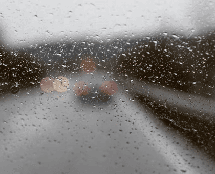 View through a rain-covered windshield showing a blurred car on a wet road.
