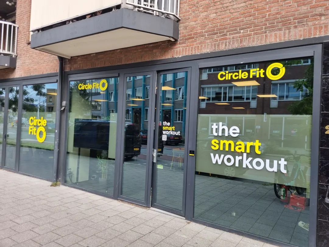 Een Circle Fit-hub met grote ramen die heldergele borden en promoties tonen, gezien vanaf het trottoir.