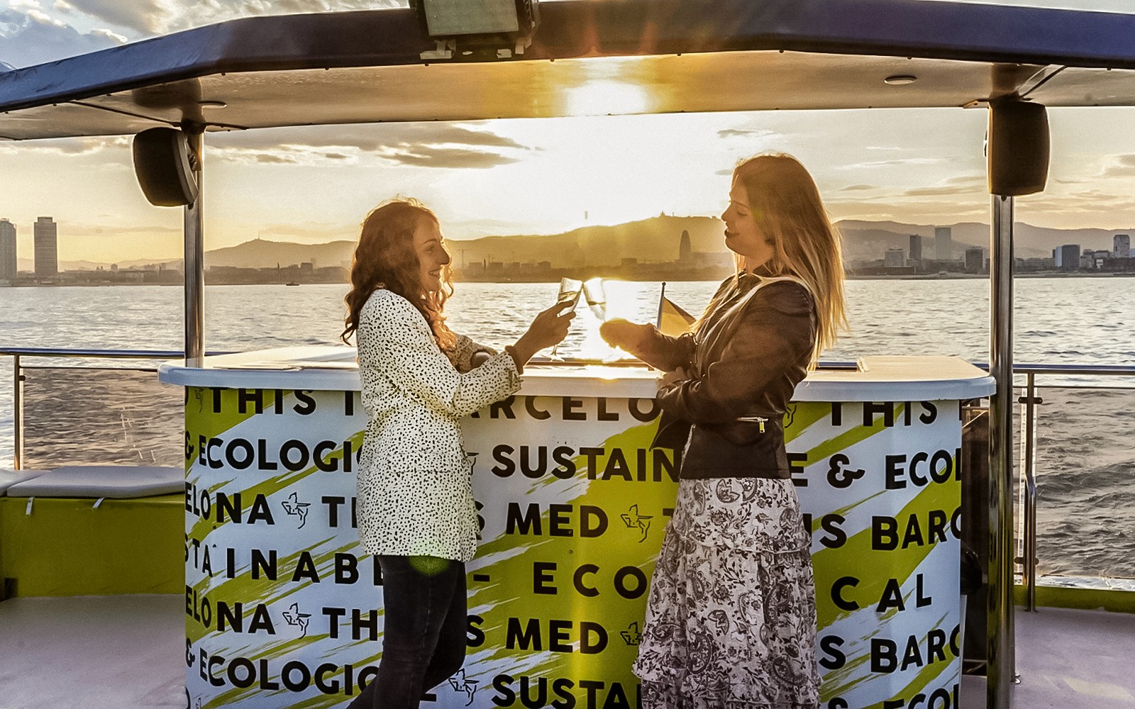 Due persone si godono un drink durante una crociera in catamarano a Barcellona al tramonto.