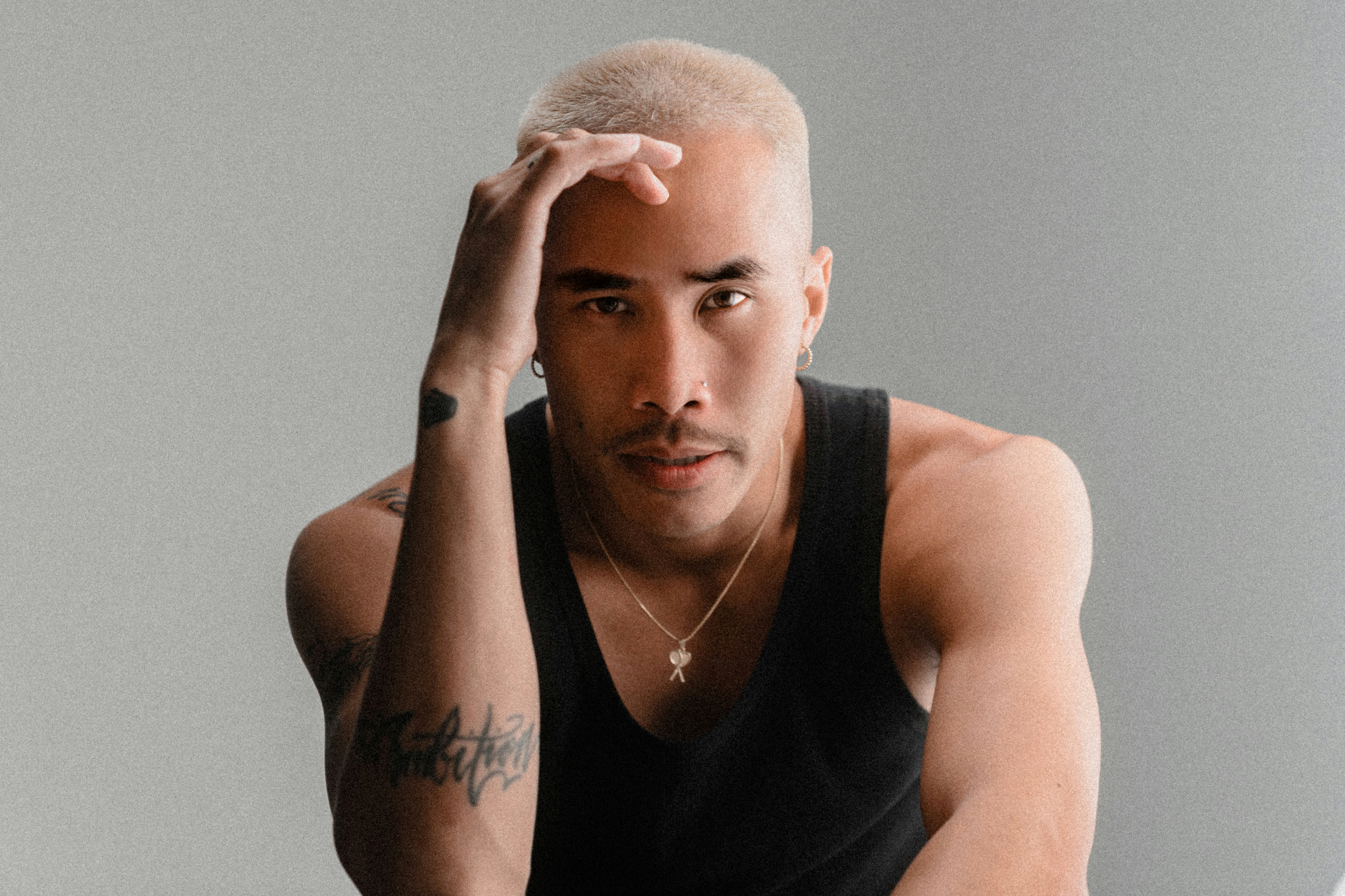 Man with blond hair and tattoos touches his head