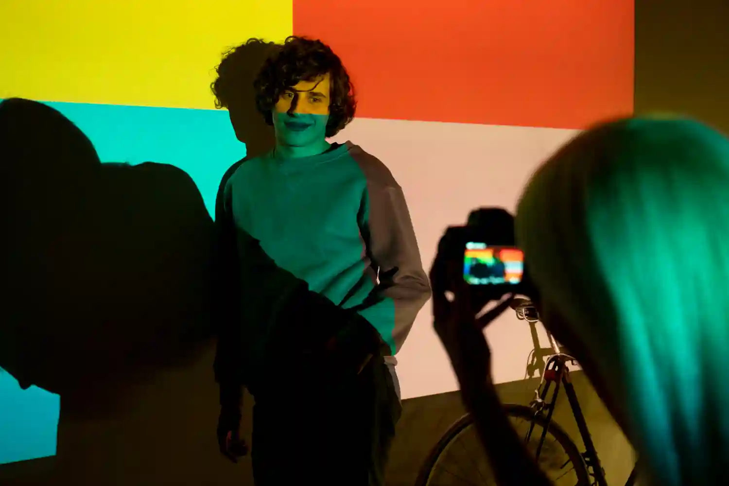A person being photographed against a background of green, yellow, and red color blocks with dramatic shadows.