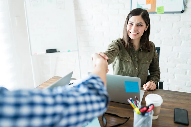 Mujer sonriente en una oficina extendiendo la mano para saludar con un apretón de manos.