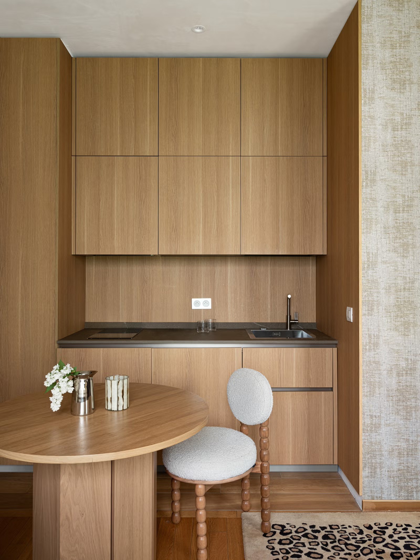 Cuisine minimaliste avec placards en bois clair sans poignées, plan de travail blanc et évier noir encastré.