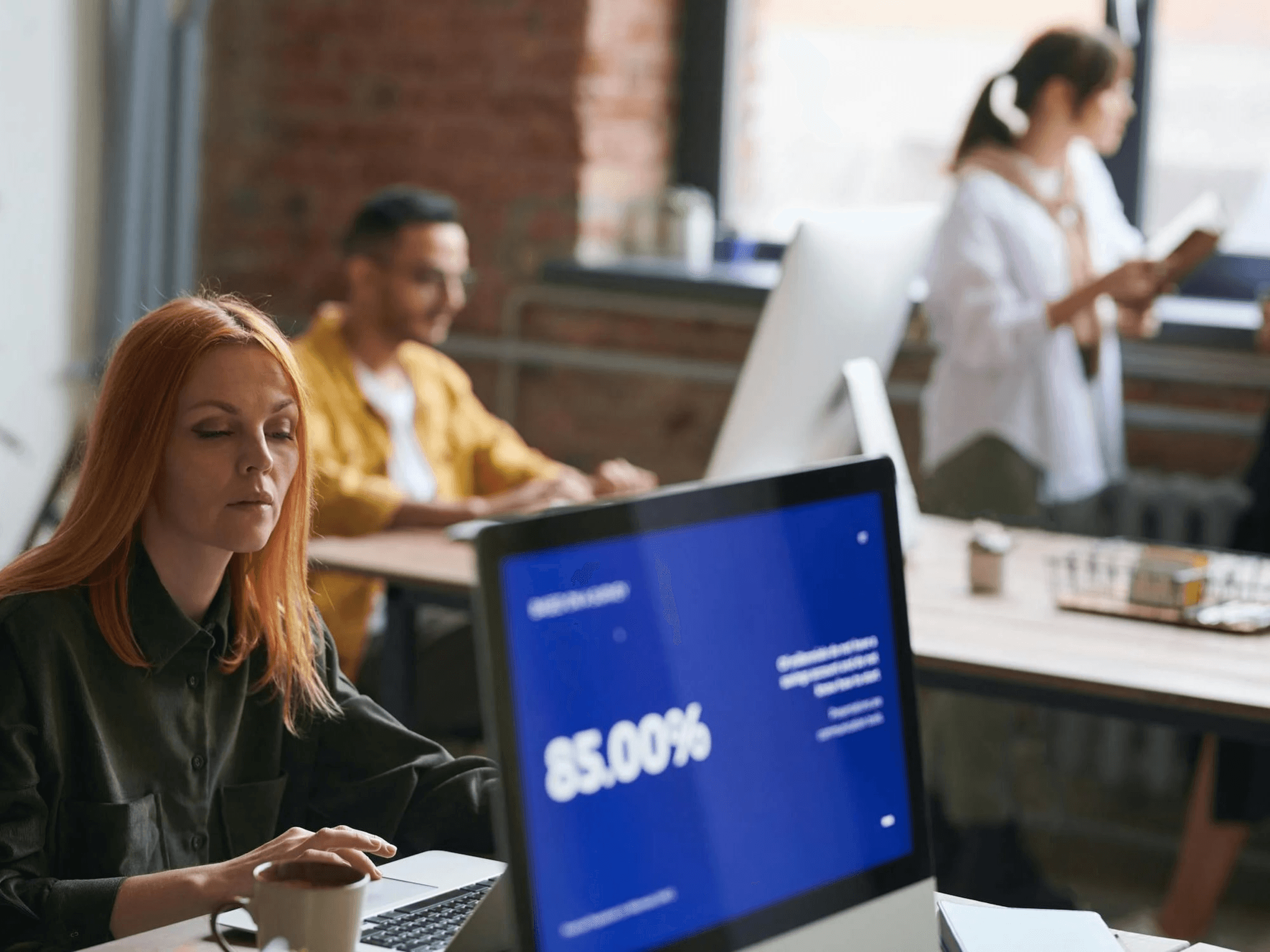 A woman with red hair is at her office computer, finding it simple to do a bank transfer using GoDutch.