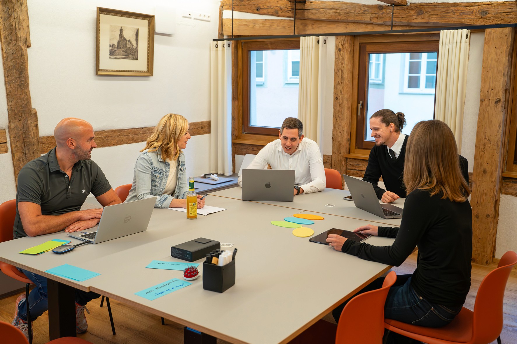 Besprechungszimmer mit einem weißen Tisch, umgeben von roten Stühlen. Elegantes Fachwerk an den Wänden.