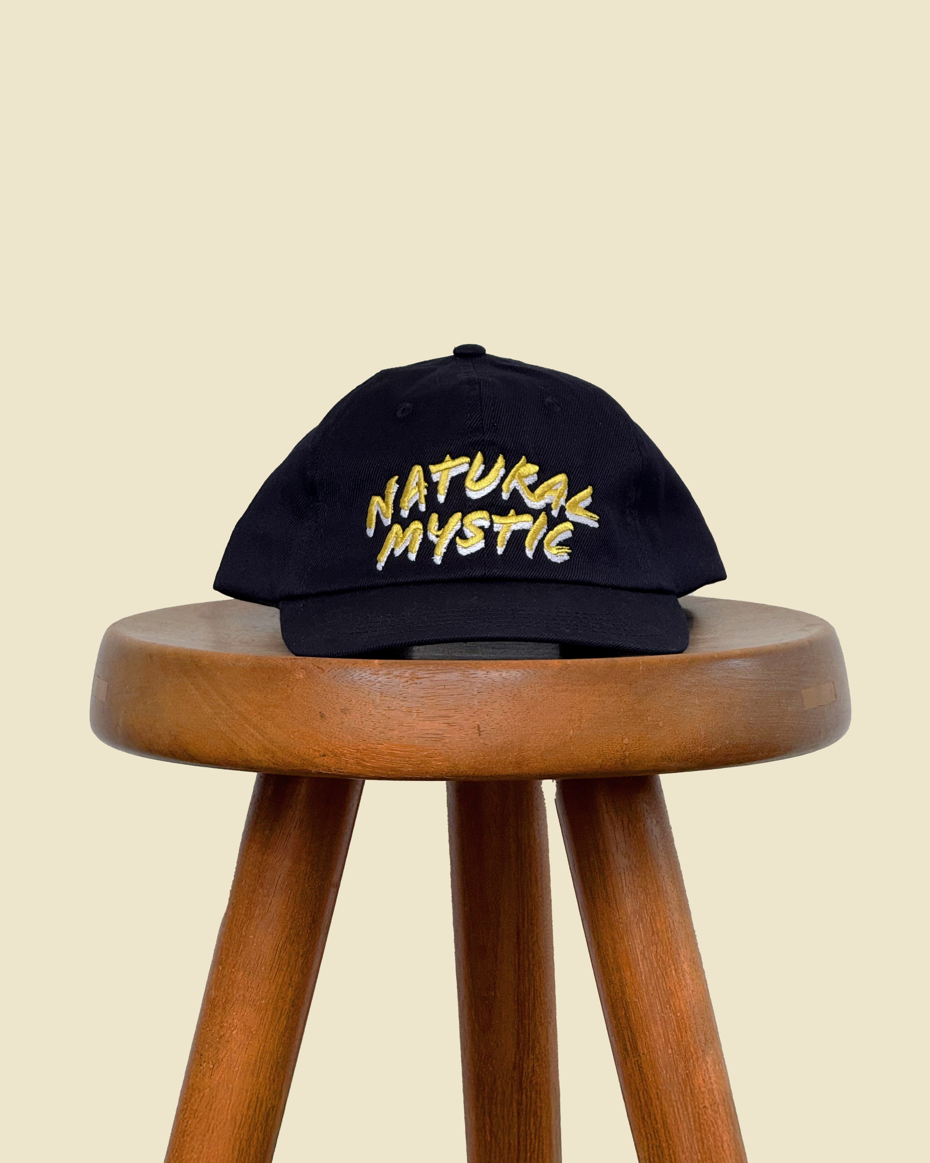 Casquette noire à message "Natural Mystic" de la marque Verlan Paris, posée sur un tabouret