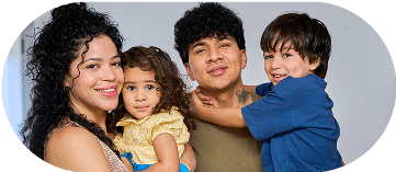 A warm, close-up portrait of a smiling family of four: a man, a woman with curly hair, and their two young children