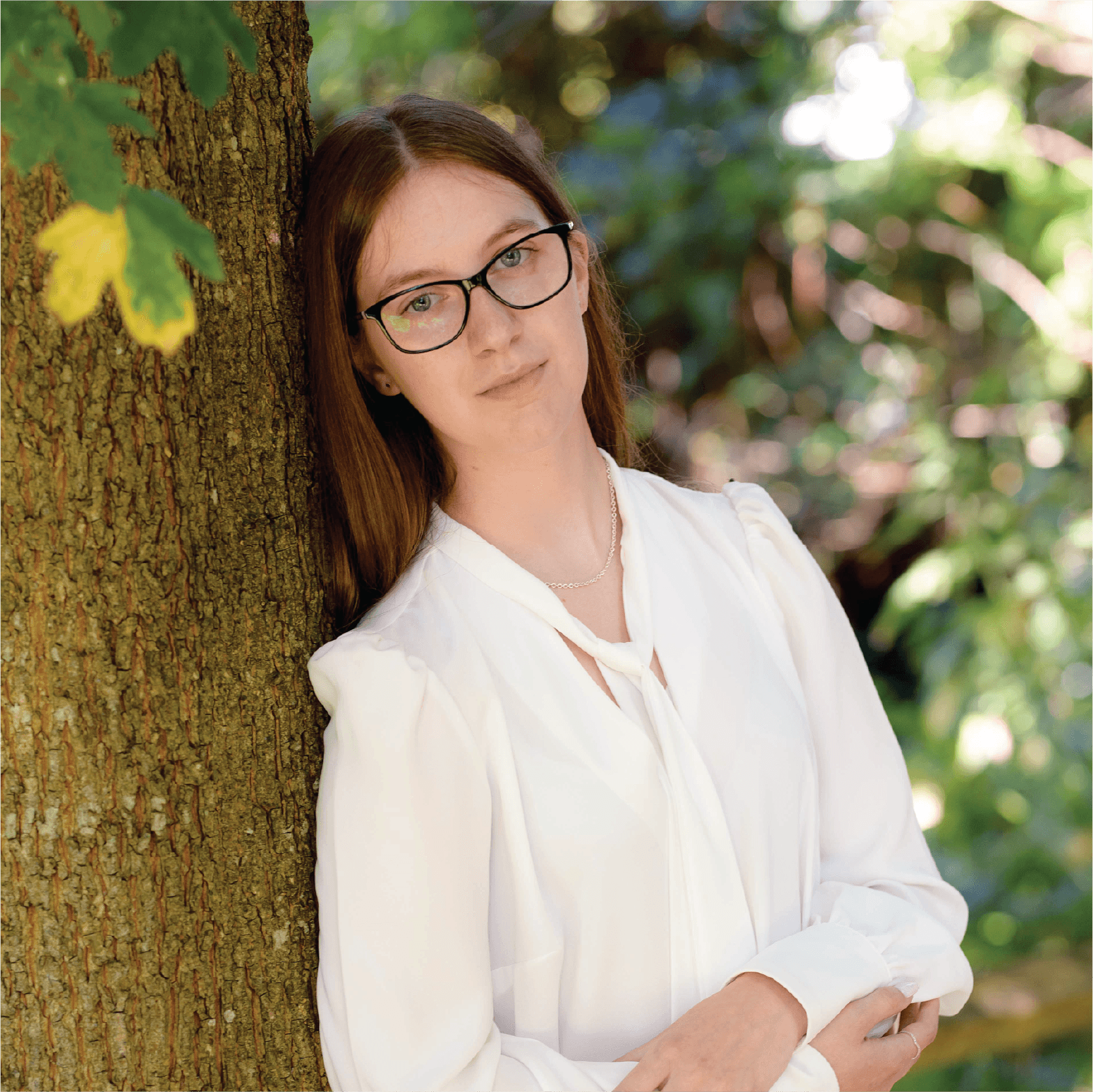 A young person with curly hair smiles at the camera while sitting in front of a laptop against a dark background.