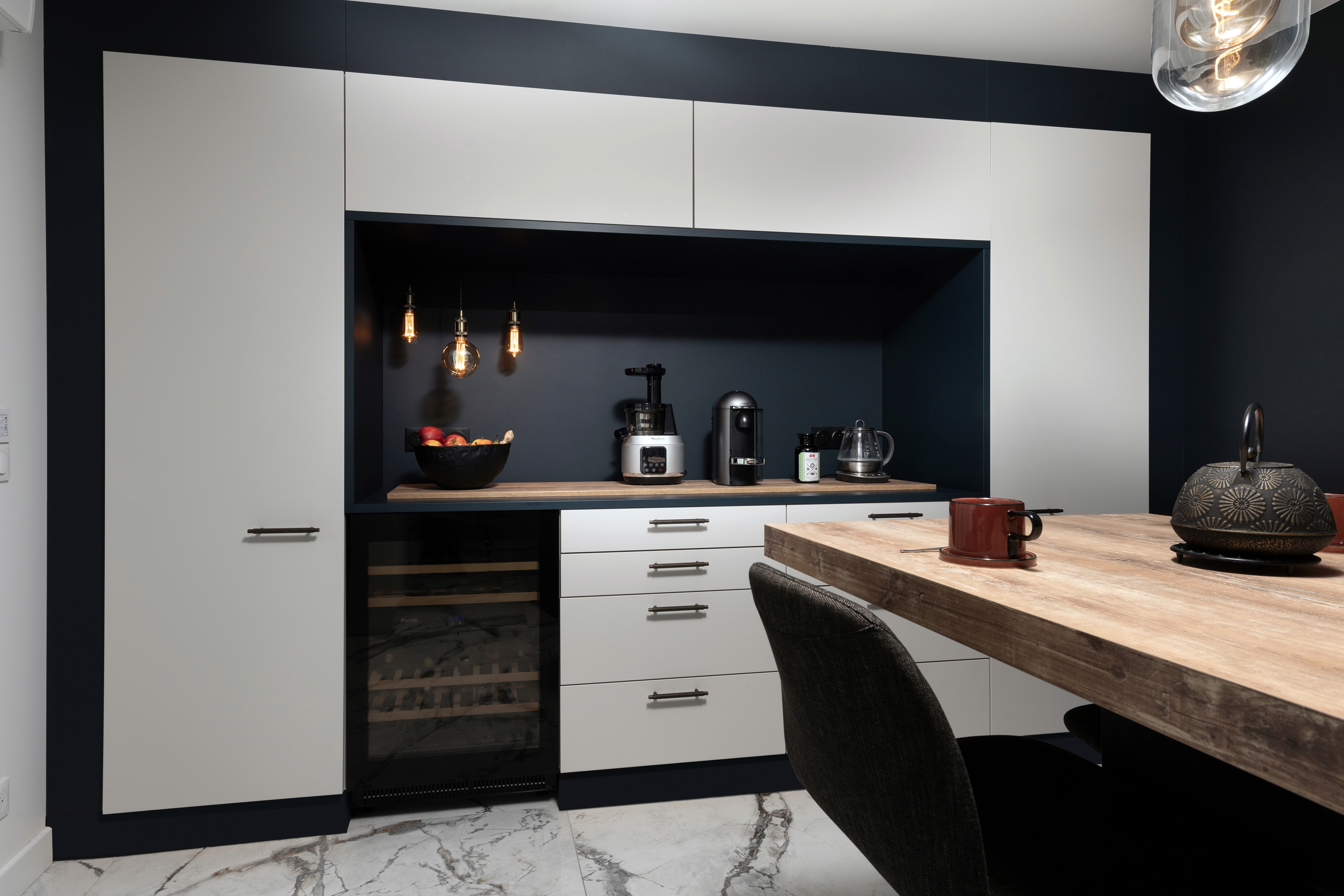Transformation cuisine Seine-et-Marne avec armoires blanches, mur accent noir, sol marbre et table salle à manger bois, rénovation 3 pièces.