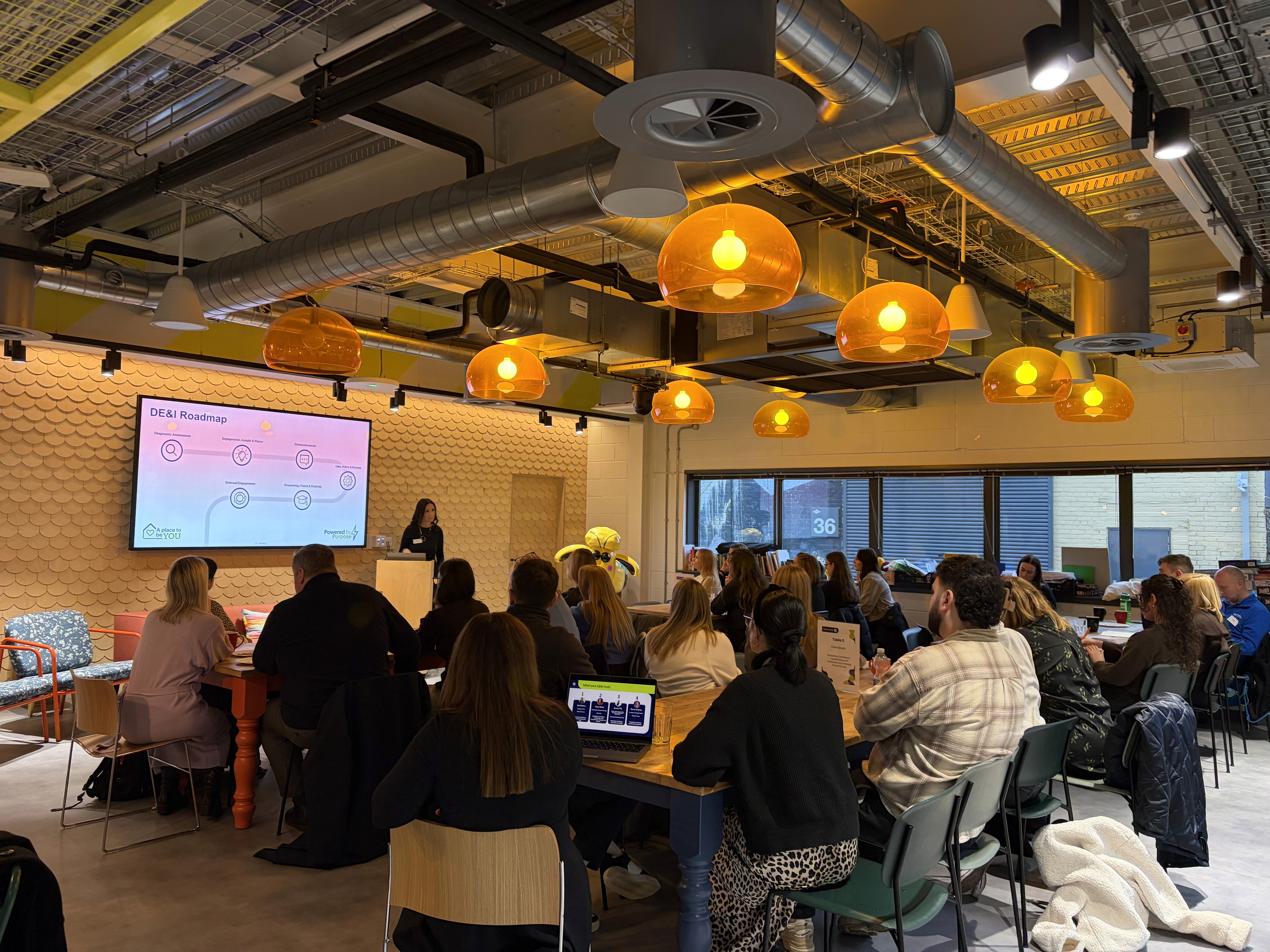 People attending a presentation in a modern meeting space with warm lighting.