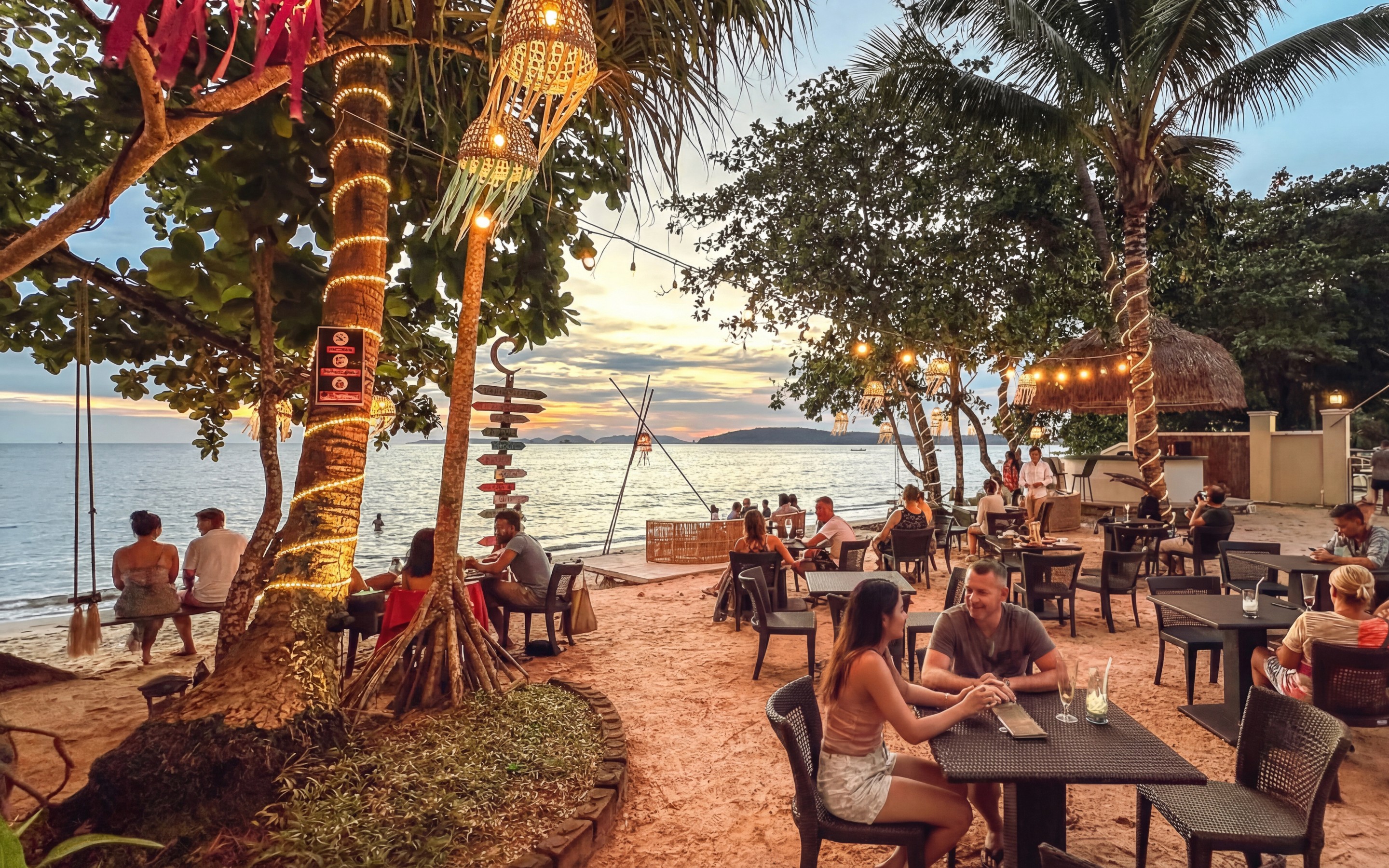 Beachfront bar and seating at sunset in Ao Nang, with people dining and drinking beside the sea.