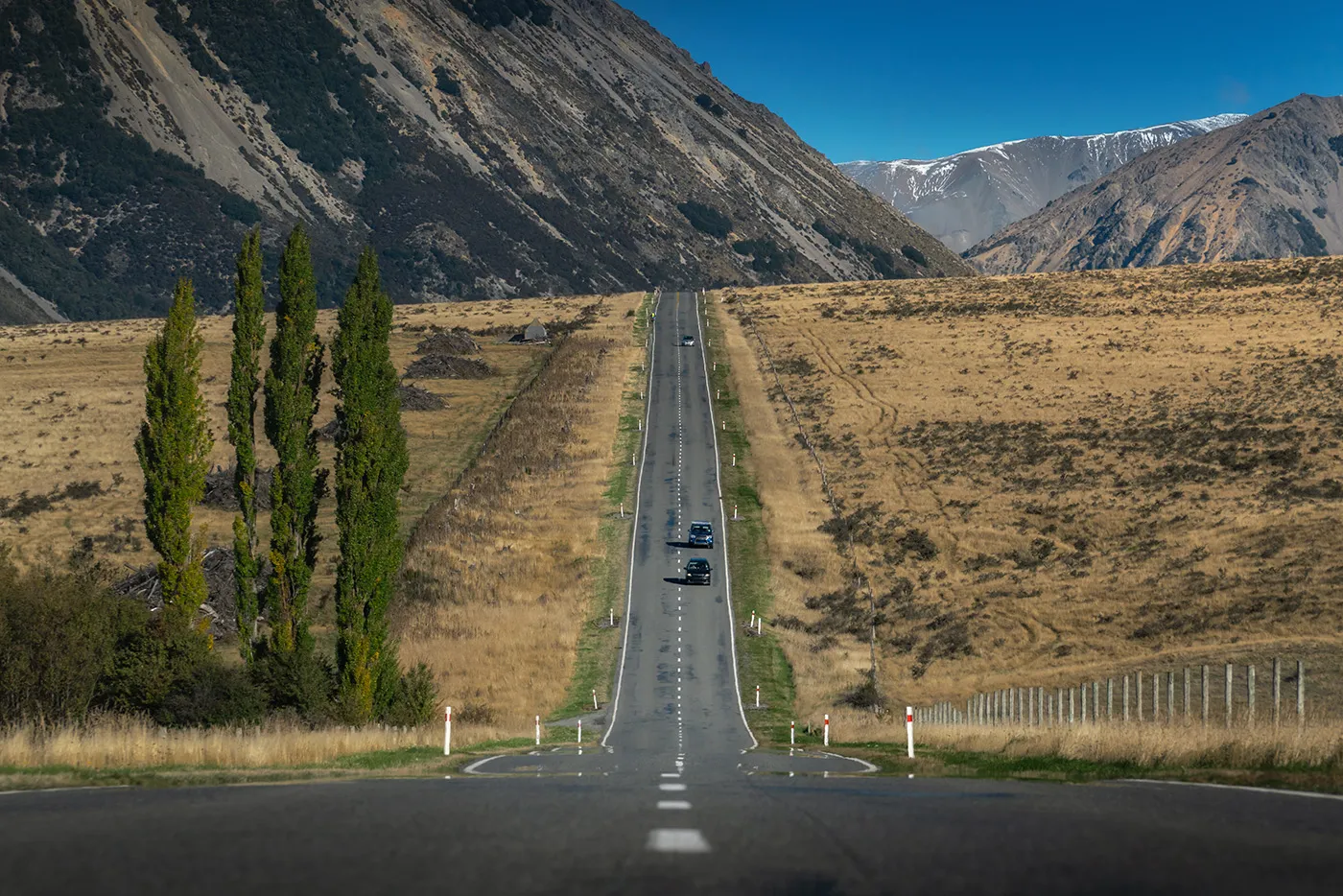 Long road in New Zealand with two cars driving towards the camera