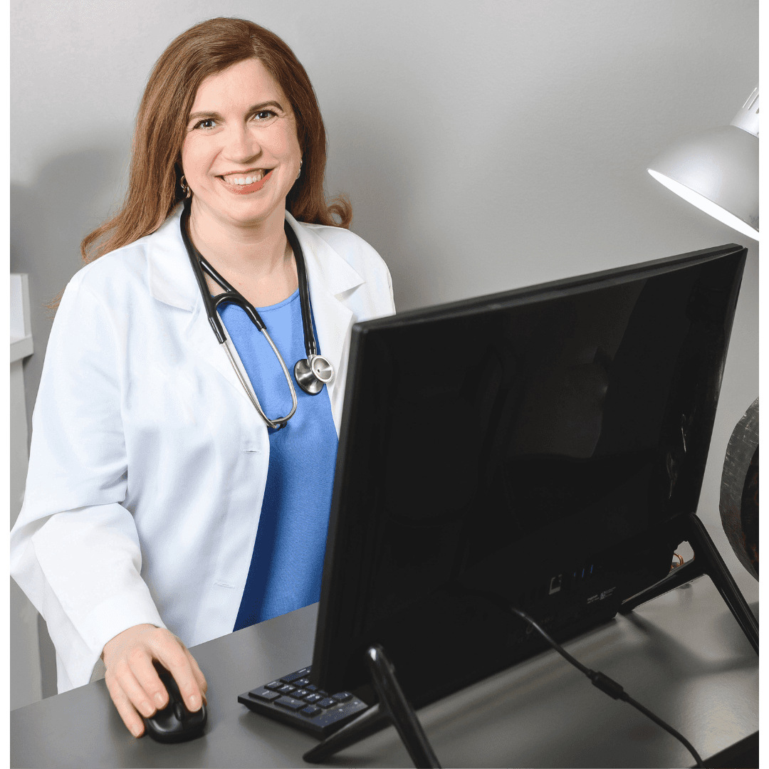 Smiling doctor at desk with computer, wearing white coat and stethoscope.