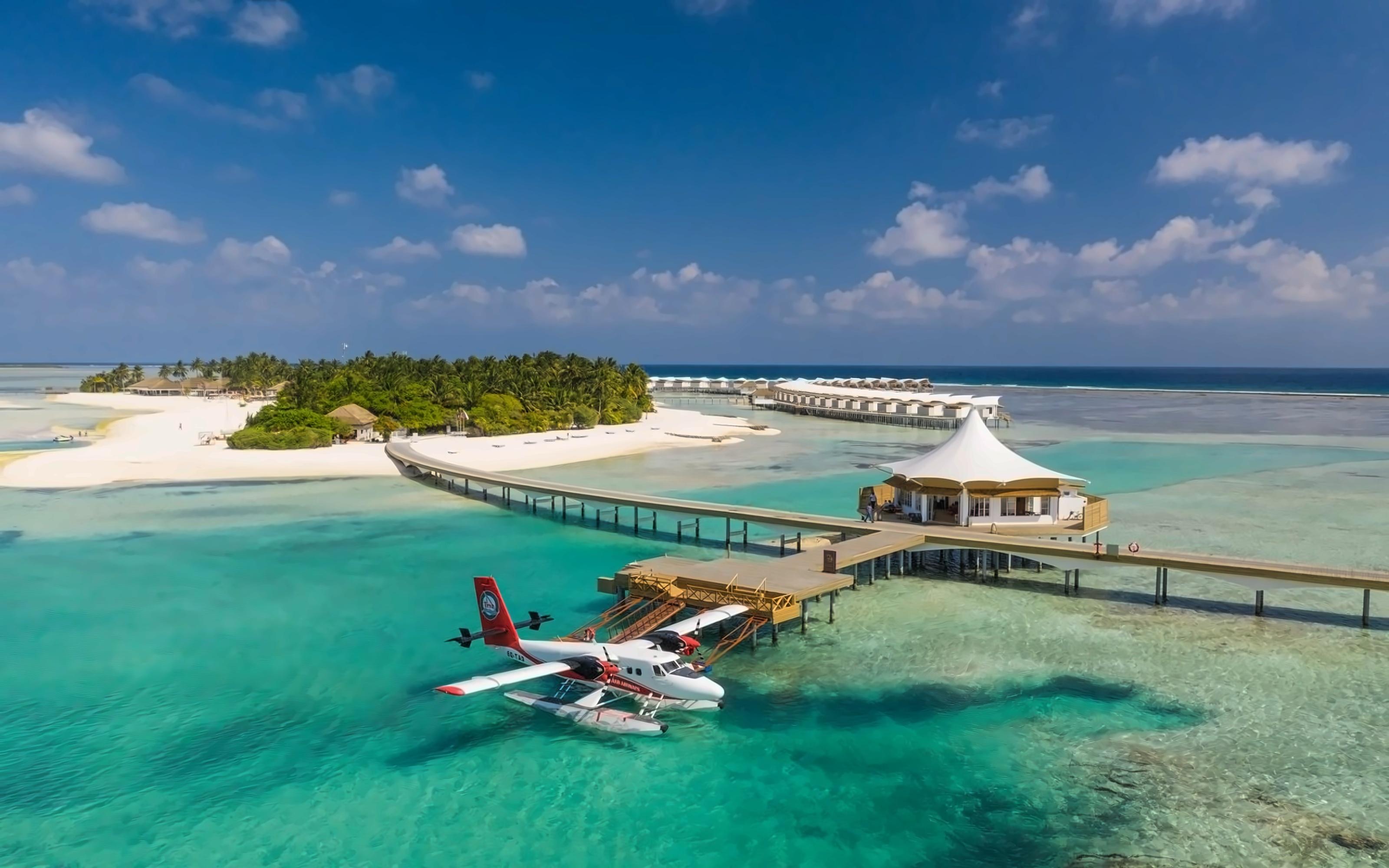 Seaplane arriving at a Maldives resort jetty over crystal-clear turquoise waters.