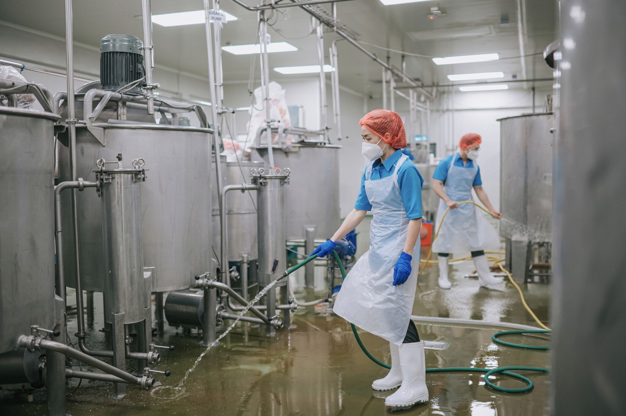 Workers in protective gear operate equipment in a clean, industrial environment, likely related to food or pharmaceuticals.