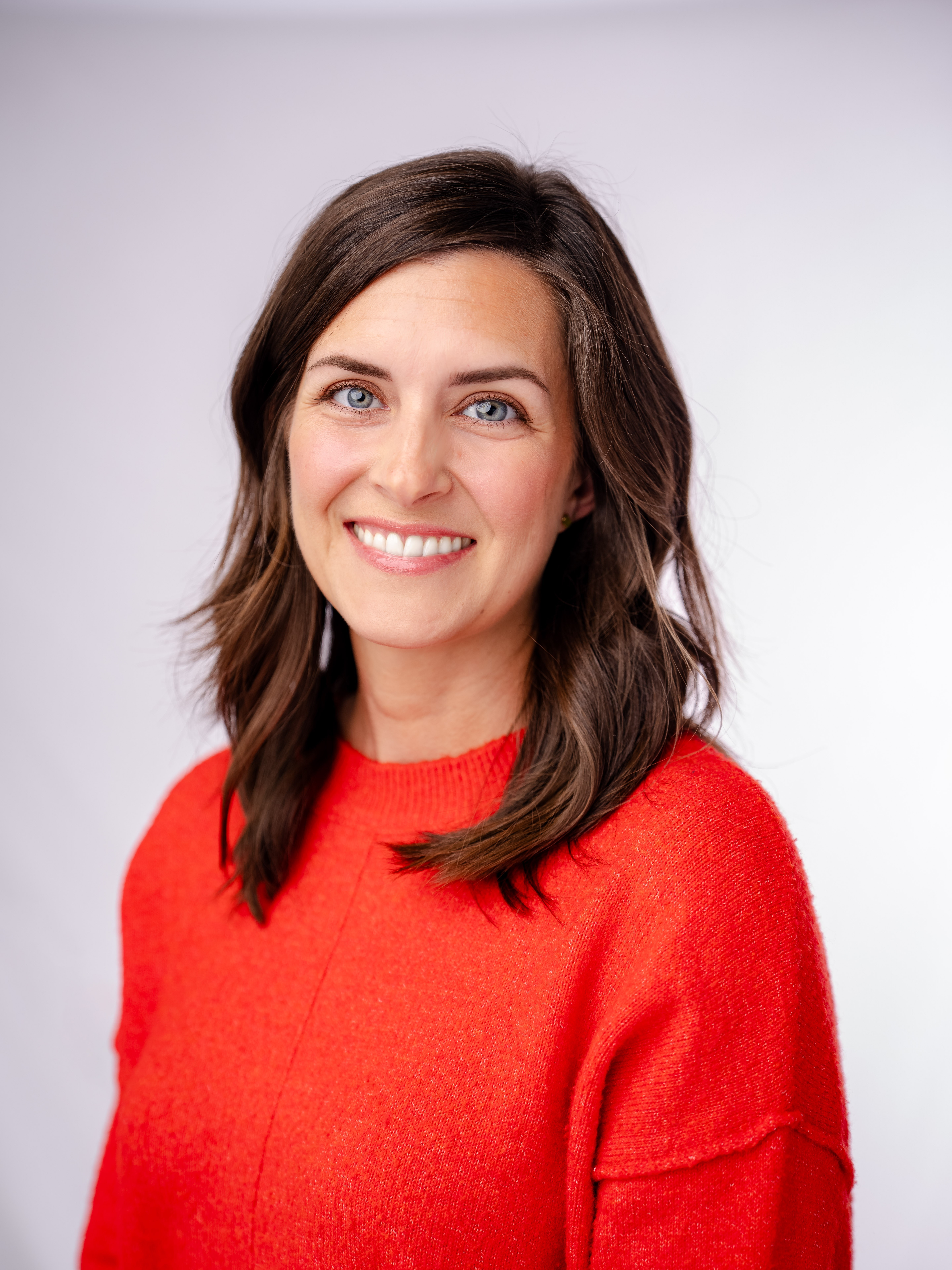 Professional headshot of Jenn Fuson, client experience and operations specialist at Dornick Wealth Management, wearing a bright red sweater and smiling in front of a light background