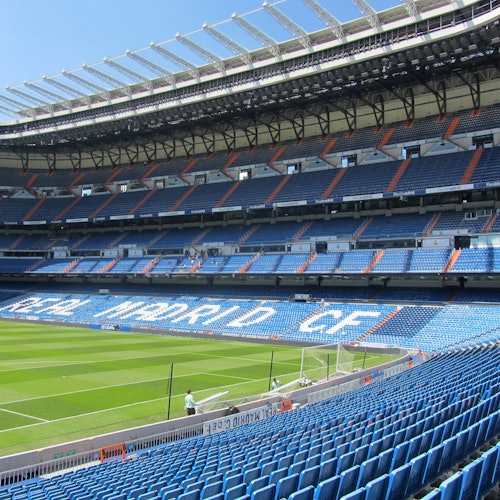 Pusty stadion piłkarski z niebieskimi siedzeniami i napisem "Real Madrid C.F.". Zielone pole i czyste niebo.