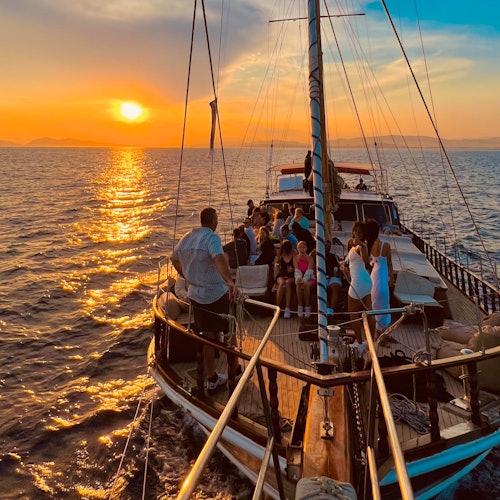 人們坐在帆船上，享受著夕陽映照在海洋上的美景，海面平靜，天空呈橙色。
