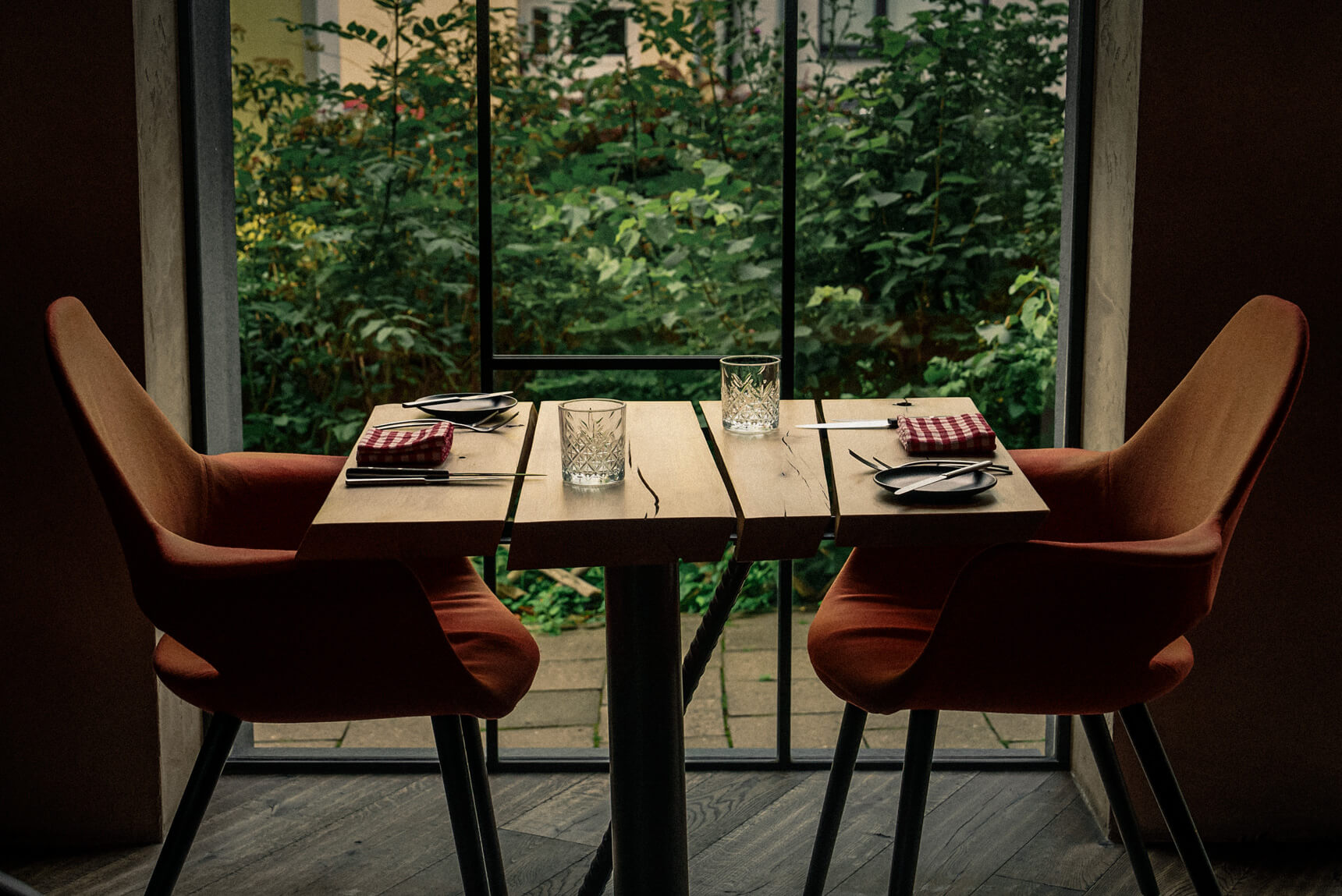 Prostřený stůl pro dva z masivního dřeva u okna s výhledem do zeleně, ideální pro romantickou večeři